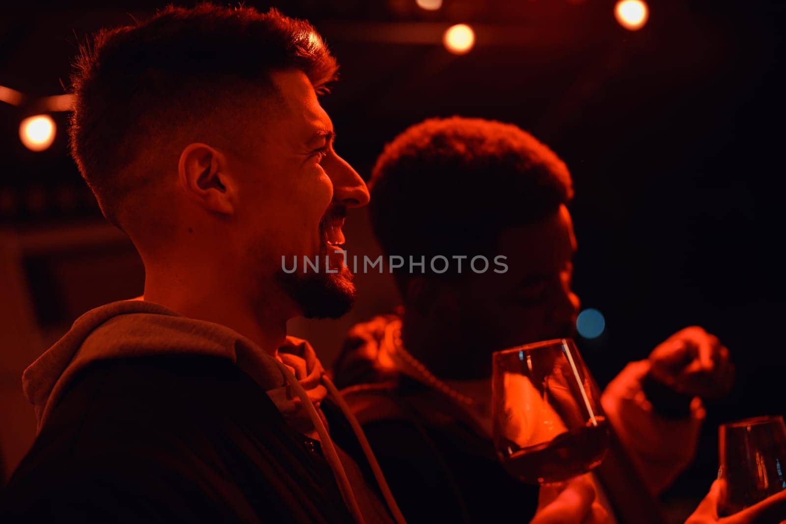 Two friends share laughter and conversation while holding glasses during a cozy evening gathering. Warm lights create a vibrant yet relaxed ambiance.
