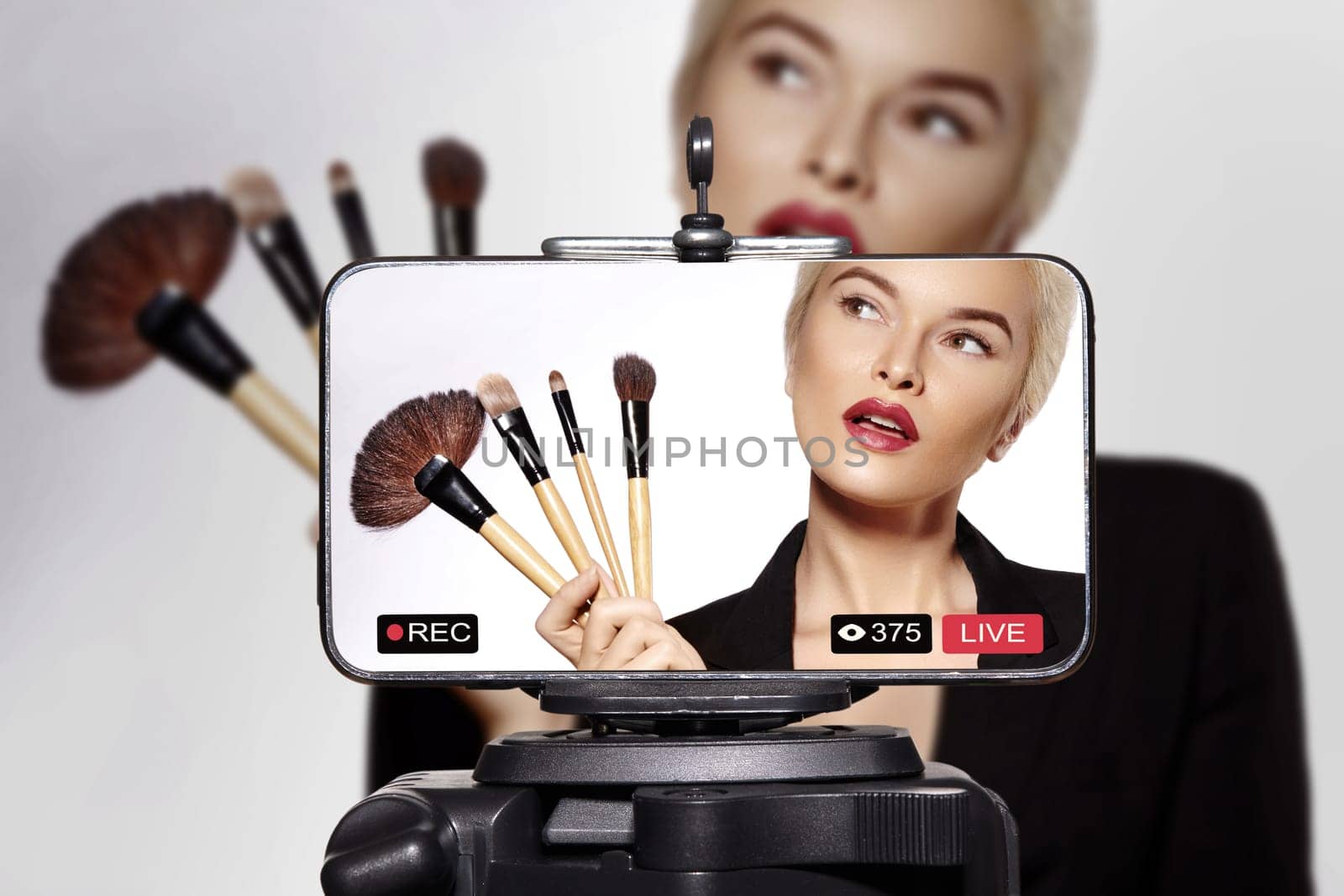 Confident woman demonstrating how apply makeup during a live beauty tutorial. Female influencer using brushes, cosmetics while teaching makeup techniques for online audience. Concept of beauty routine, self-makeup, and social media content creation