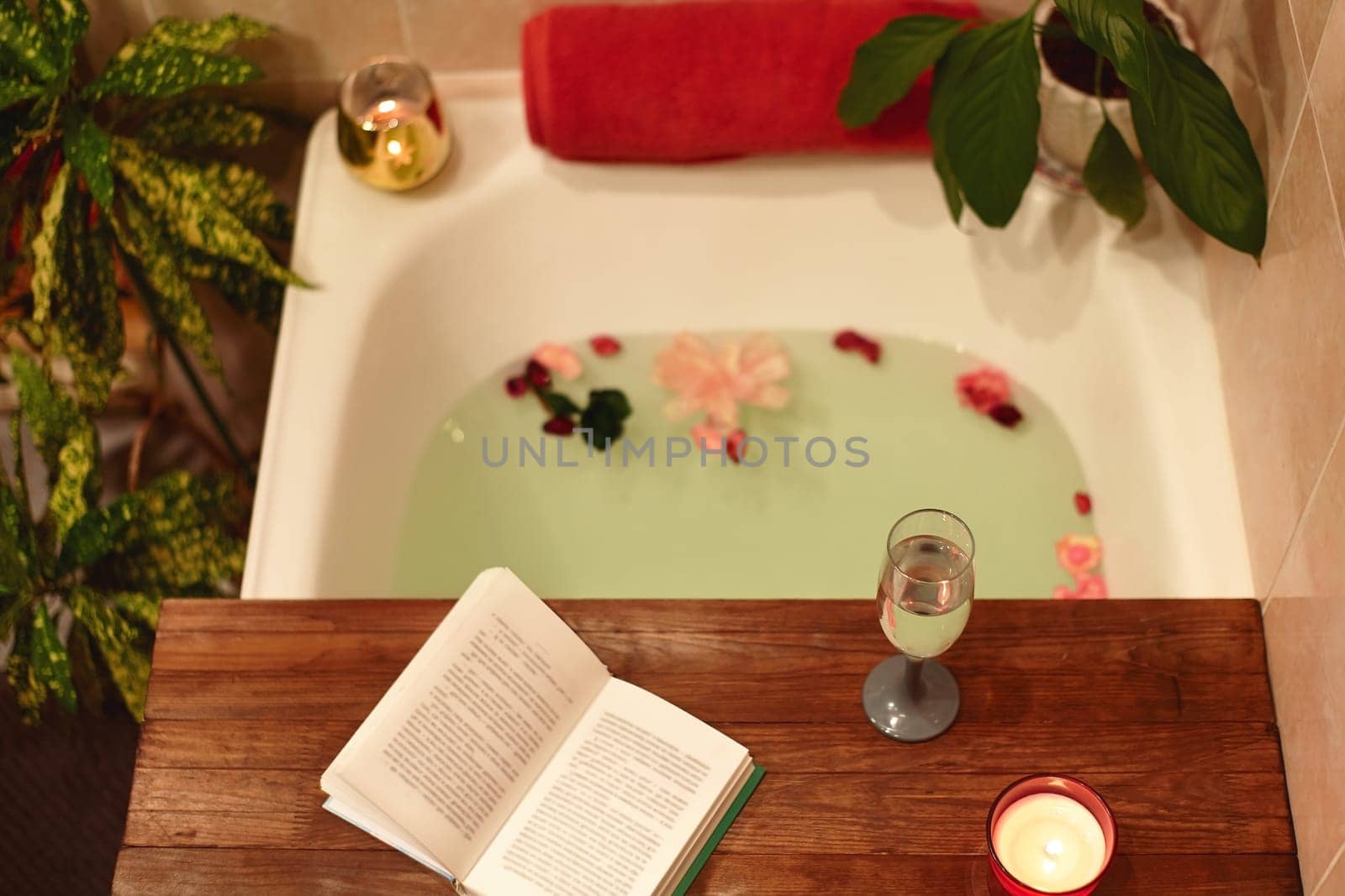 Time for Yourself. Relax at home. Bath tub with flower petals. Book, candles and glass of wine on a wood tray. Organic Spa Relaxation in comfort cozy bathroom