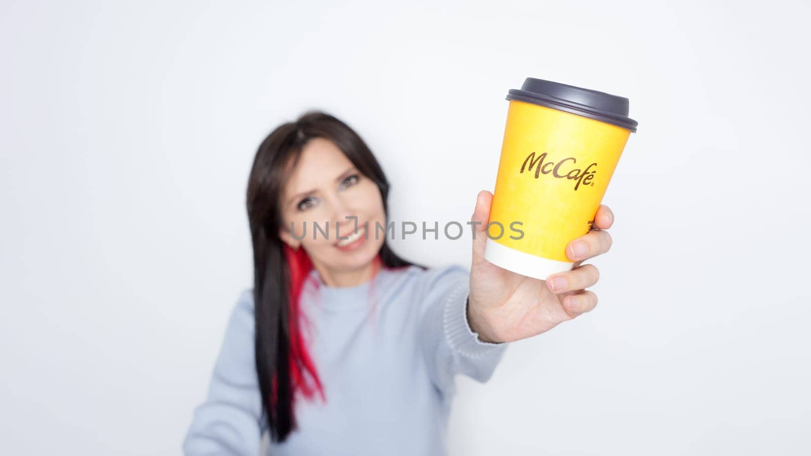 Ottawa ON Canada -2024-10-28: Cheerful woman with long dark hair holding McDonalds yellow coffee cup joyfully on white background.