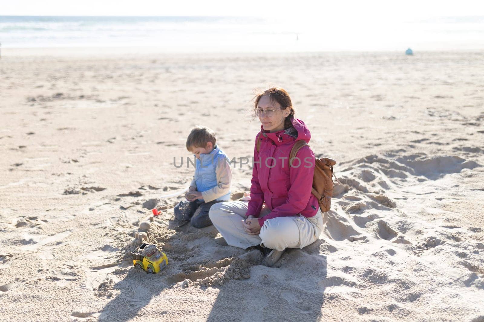 Mother and son enjoying a relaxing day at the beach, playing with sand and toy trucks
