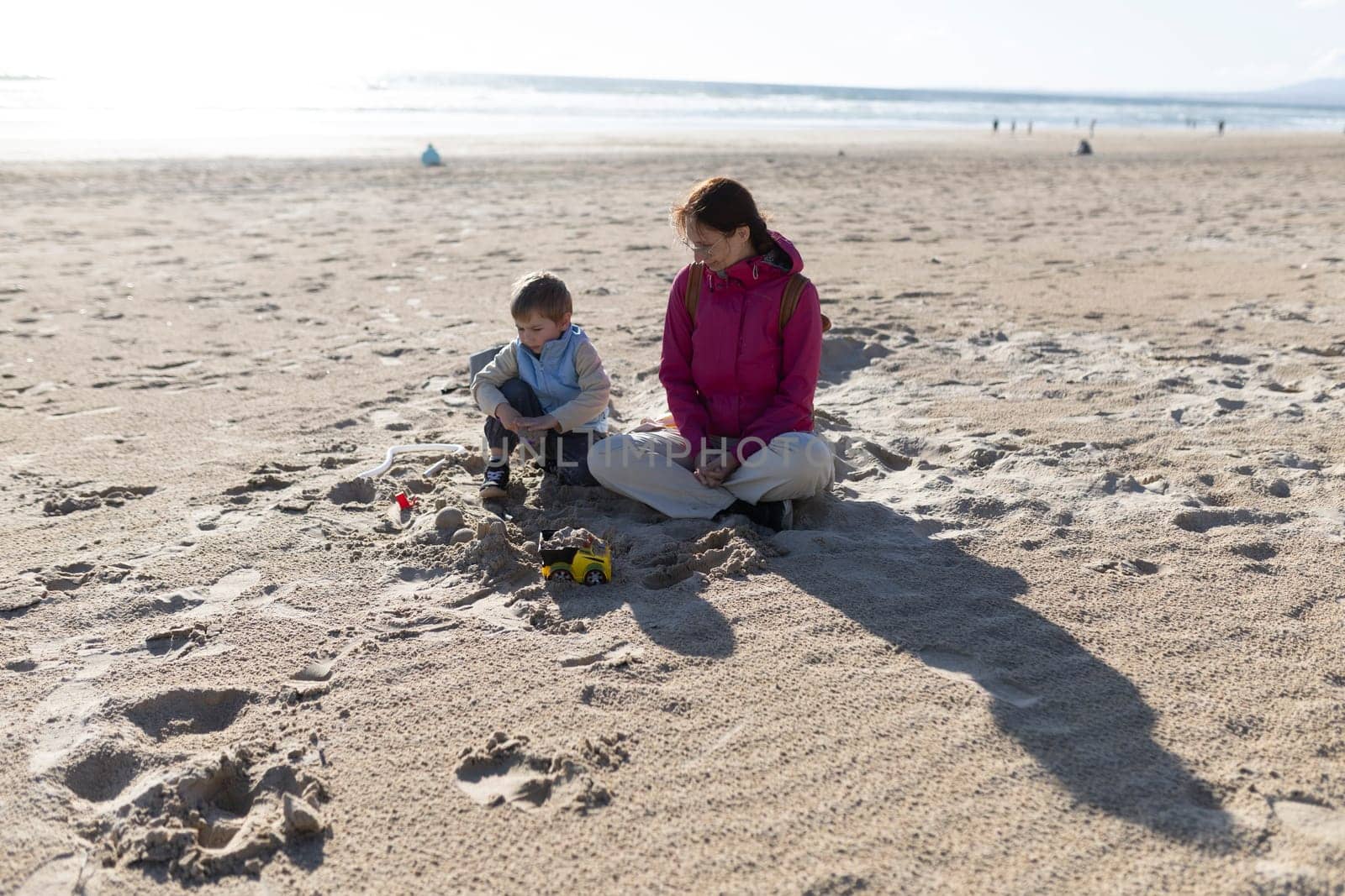 Mother and son enjoying quality time together, sitting on a sandy beach and playing with toys