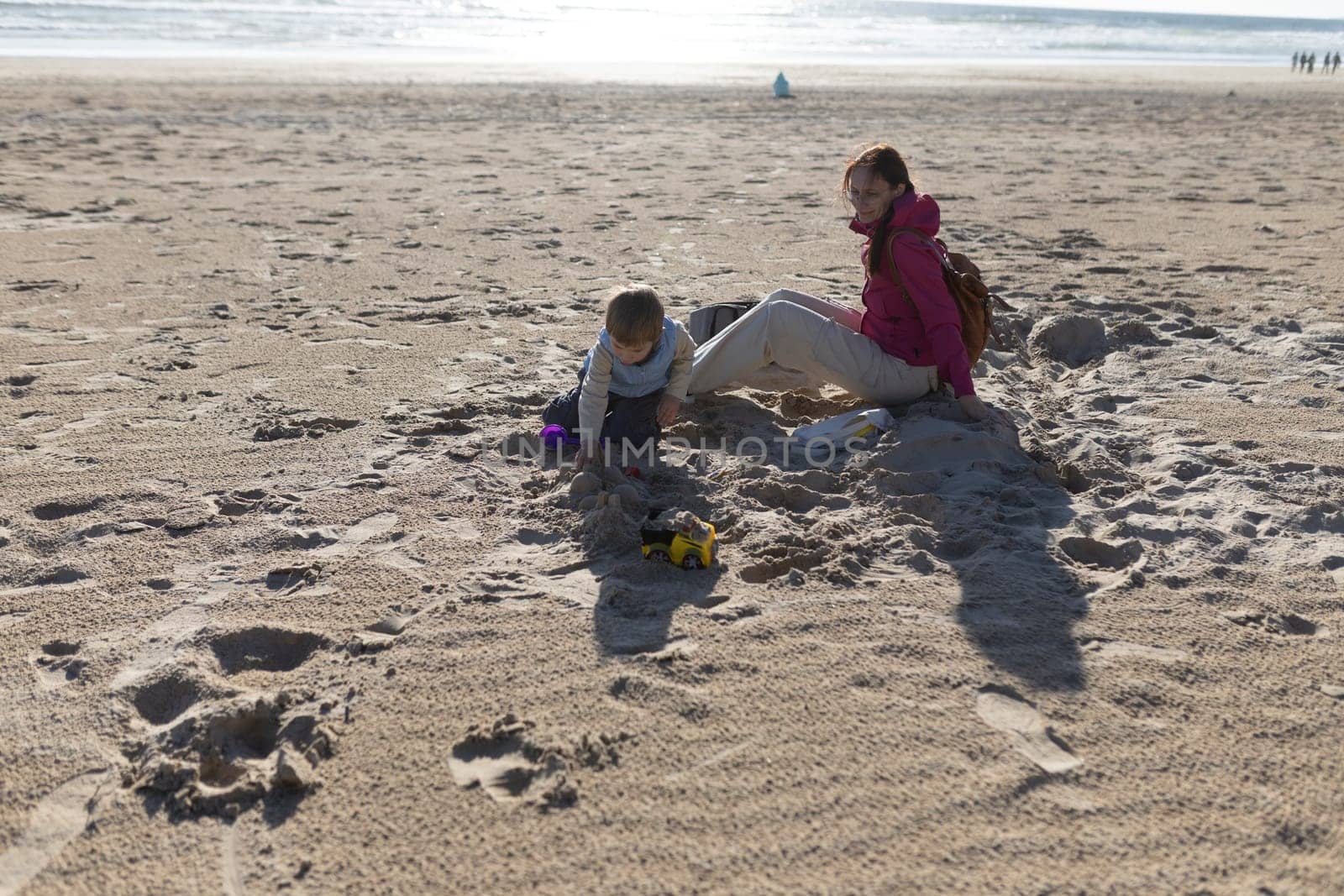 Mother watching her son playing with sand on the beach on a sunny day