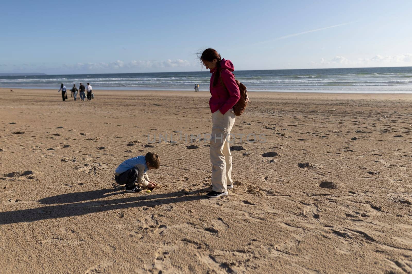 Mother watching her son playing on the sand on a sunny beach