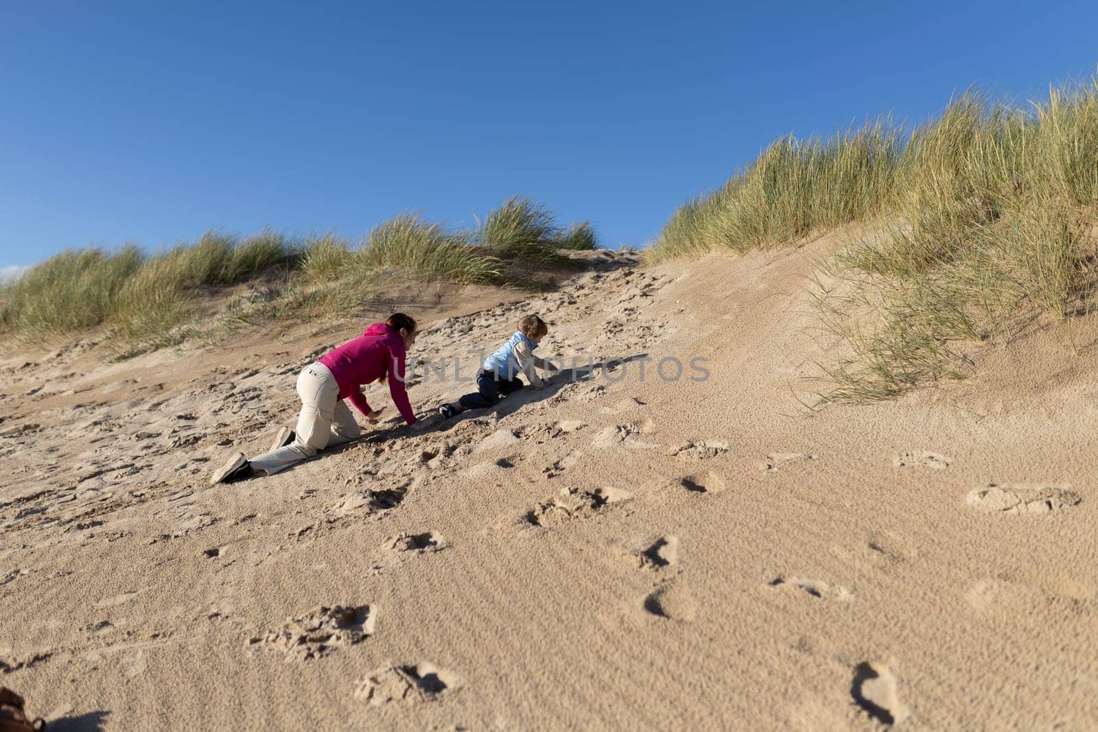Mother and son playing crawling up a sandy dune on the beach on a sunny day