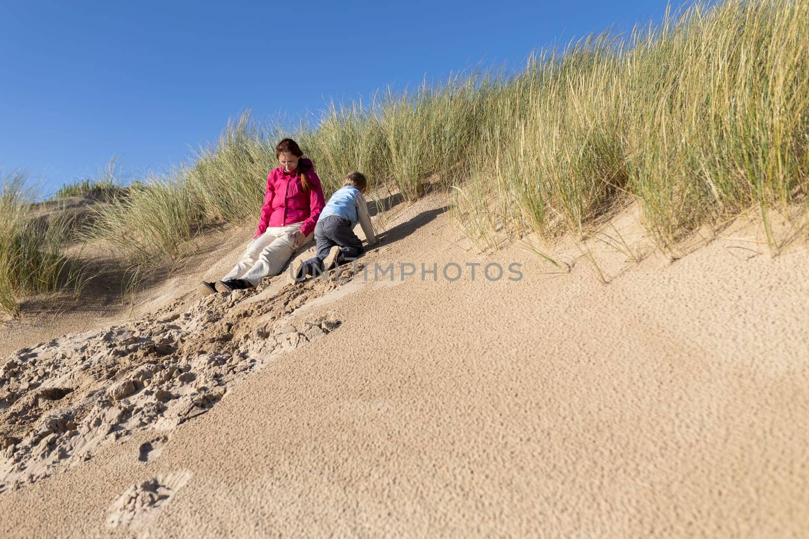 Mother and son having fun sliding down a sand dune on a sunny day at the beach