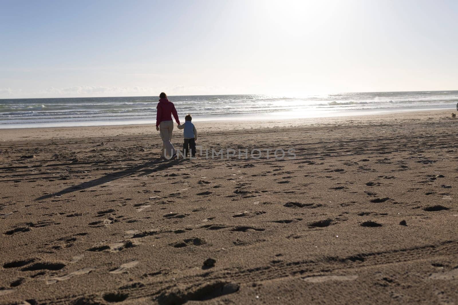 Mother and son enjoying a leisurely stroll along a sandy beach at sunset