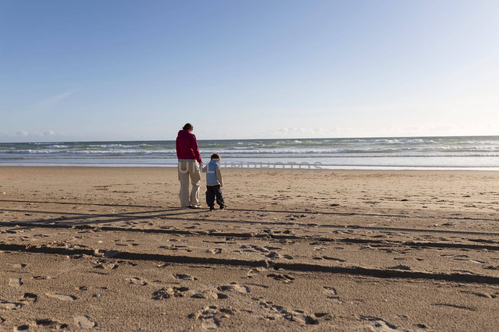 Mother and son holding hands, enjoying a relaxing walk on a beautiful sandy beach by the ocean