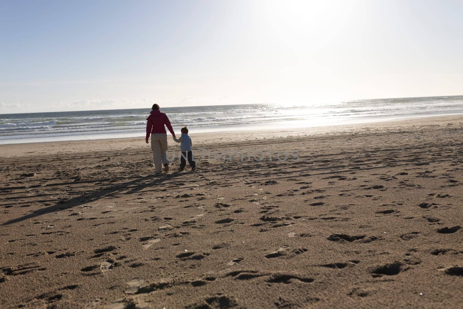 Mother and son holding hands walking on a beach towards the ocean at sunset