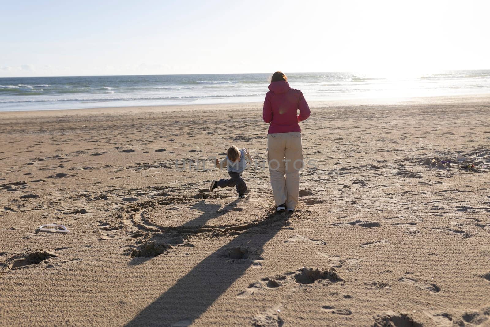 Mother and son drawing circle in sand on beach at sunset