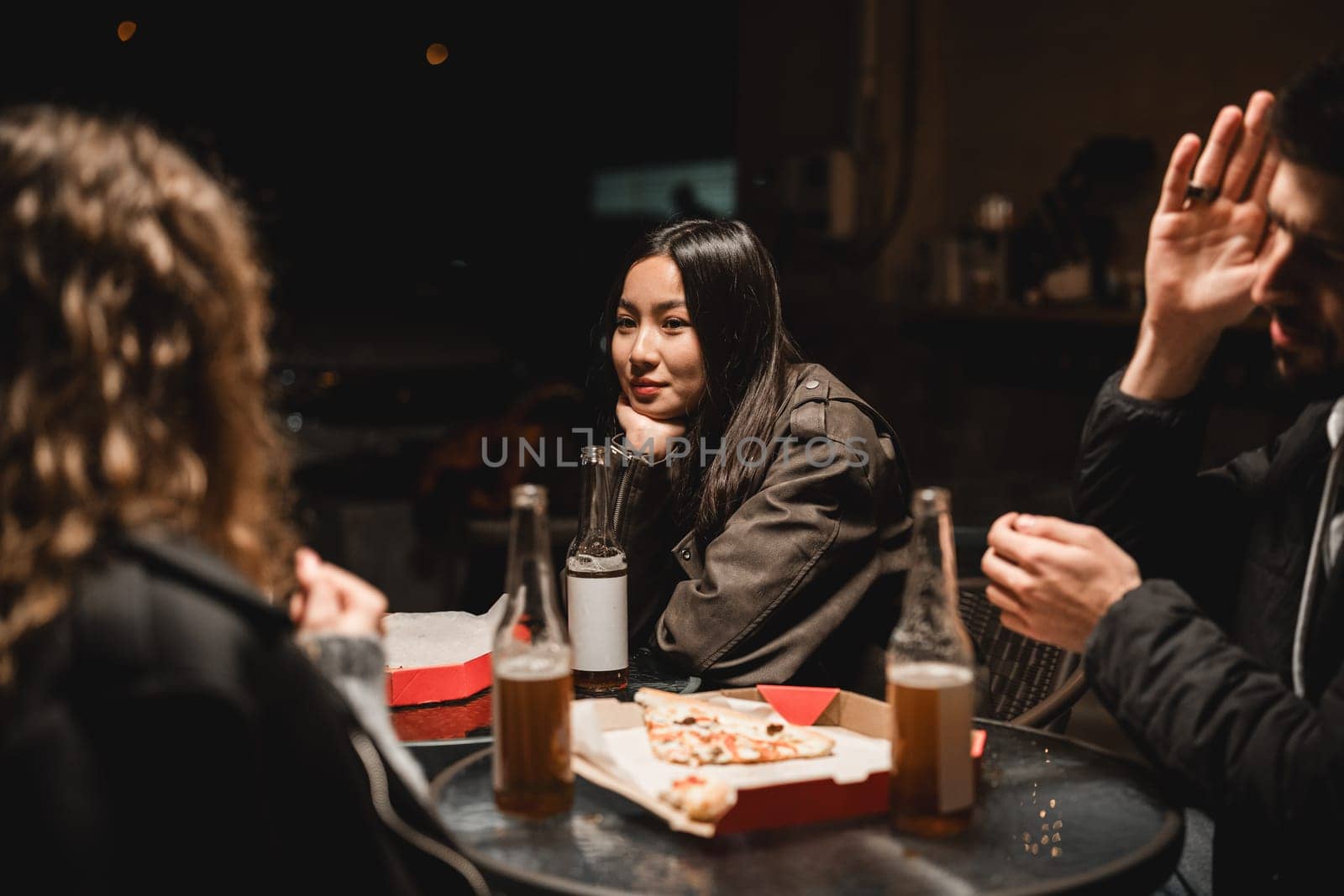 Group of friends share laughs over pizza and drinks at an outdoor table in the evening. The atmosphere is relaxed and friendly, highlighting their connection.