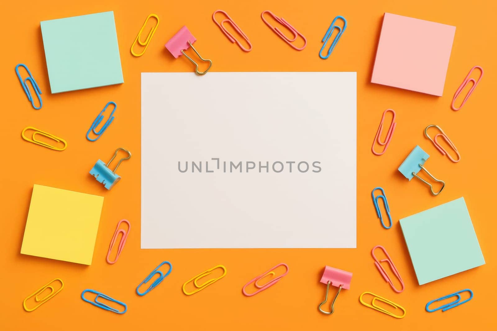 Colorful flat lay of office supplies with sticky notes, binder clips, and paper clips on an orange background. Back-to-school promotions, organizational visuals, or creative stationery layouts.