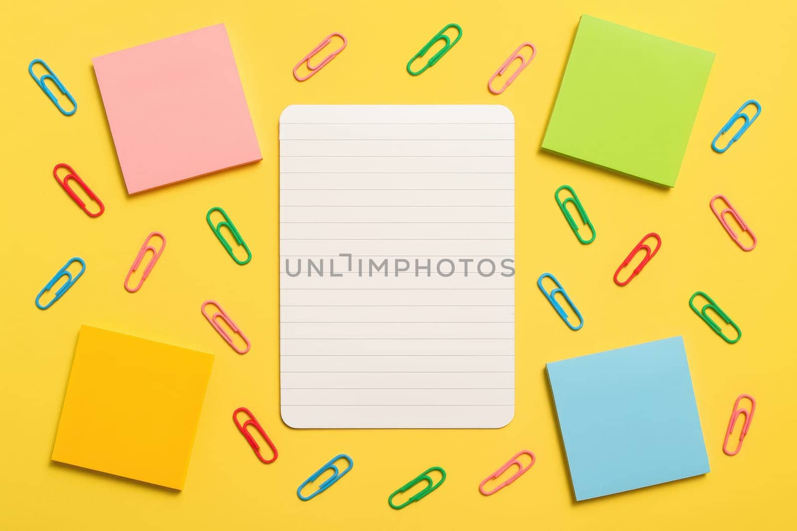 Top view of a notebook sheet with colorful sticky notes and scattered paper clips on a yellow background. Great for school designs, planning visuals, back-to-school themes and organizational content
