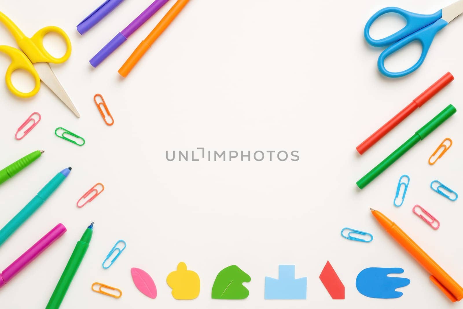 Flat lay of assorted school stationery including pens, scissors, paper clips, and fun shapes on a clean white background. Ideal for educational, creative, or promotional uses