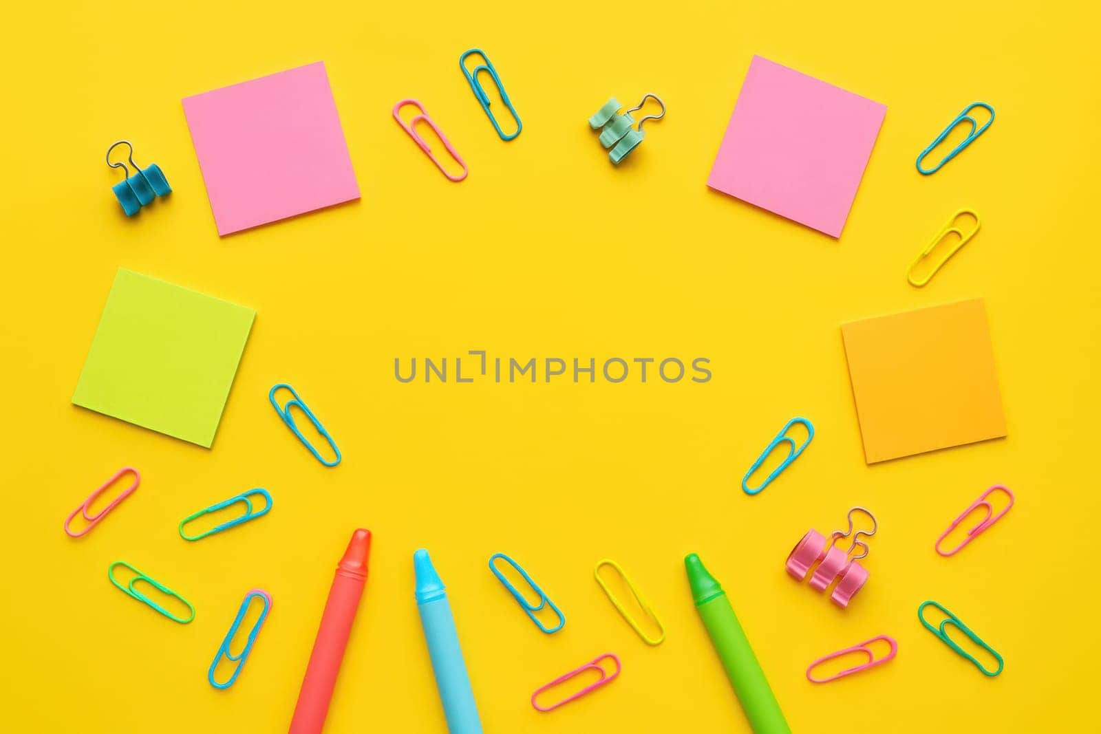 Brightly colored school supplies such as crayons, paper clips, and sticky notes scattered on a yellow background. Ideal for educational themes, creative visuals, and back-to-school designs