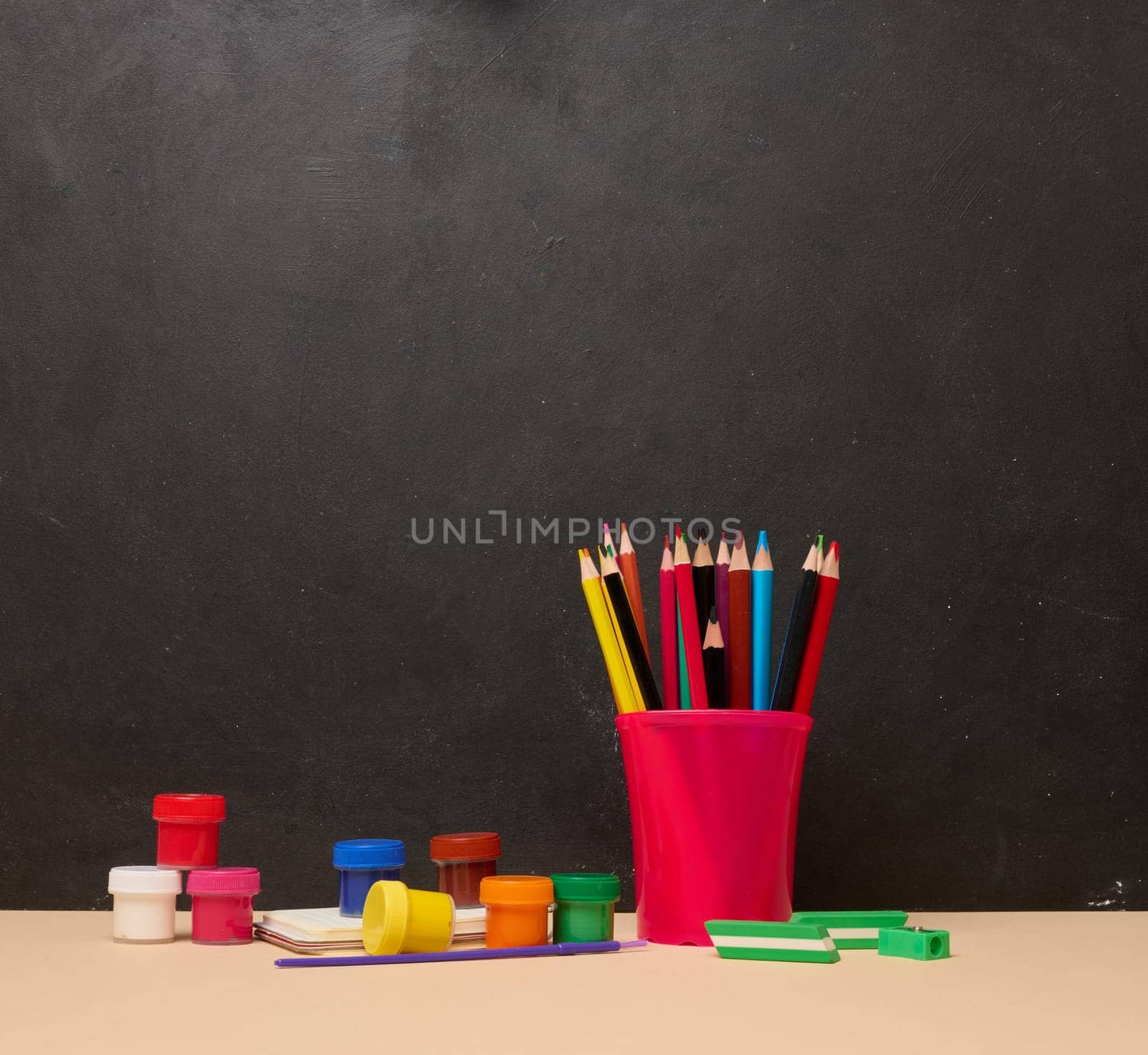 Pink glass with writing utensils, paint cans, brush, creativity or school activities