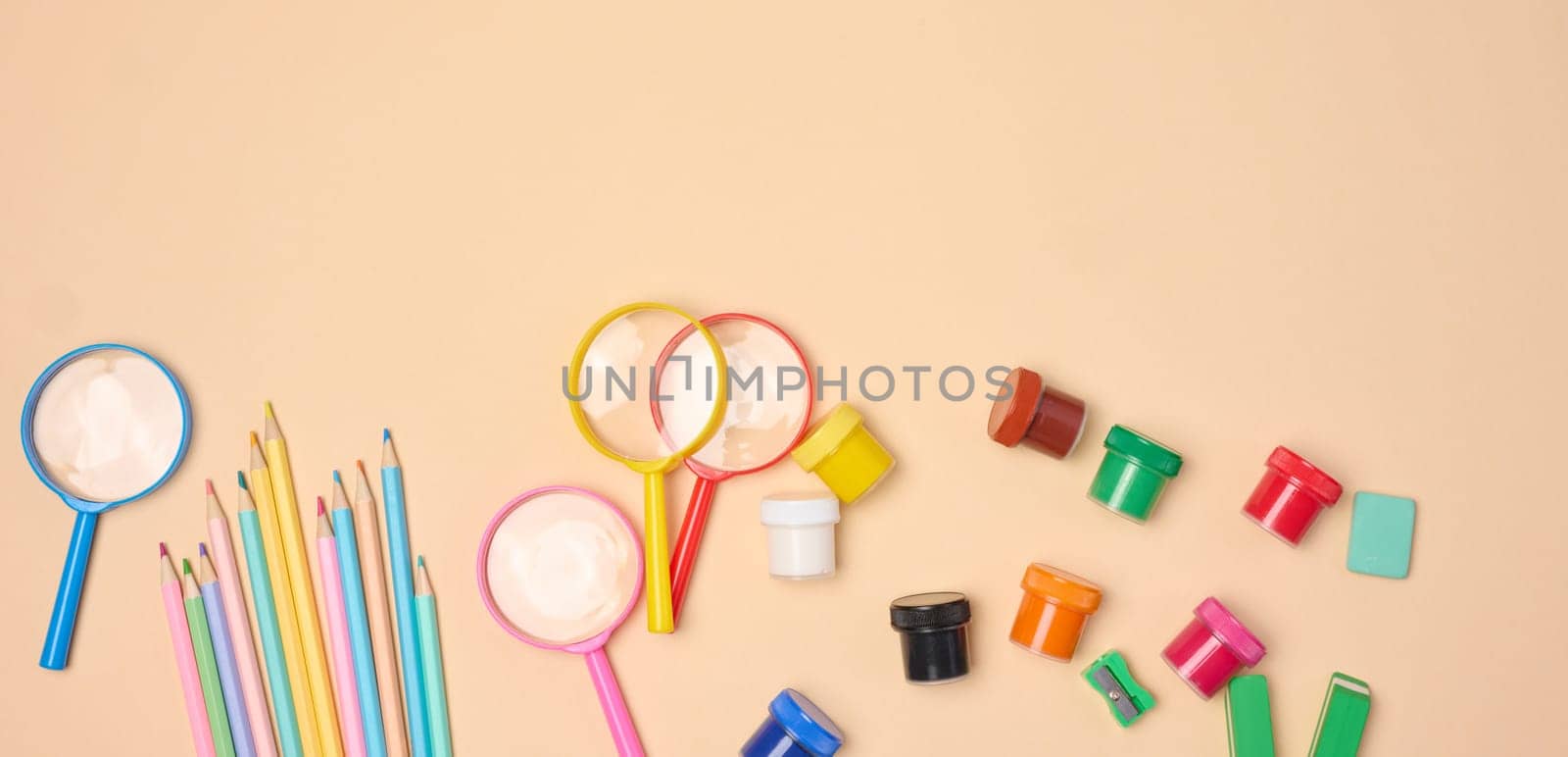 A collection of brightly colored school and office supplies, including pencils, magnifying glasses, paper clips and erasers, scattered on a neutral background