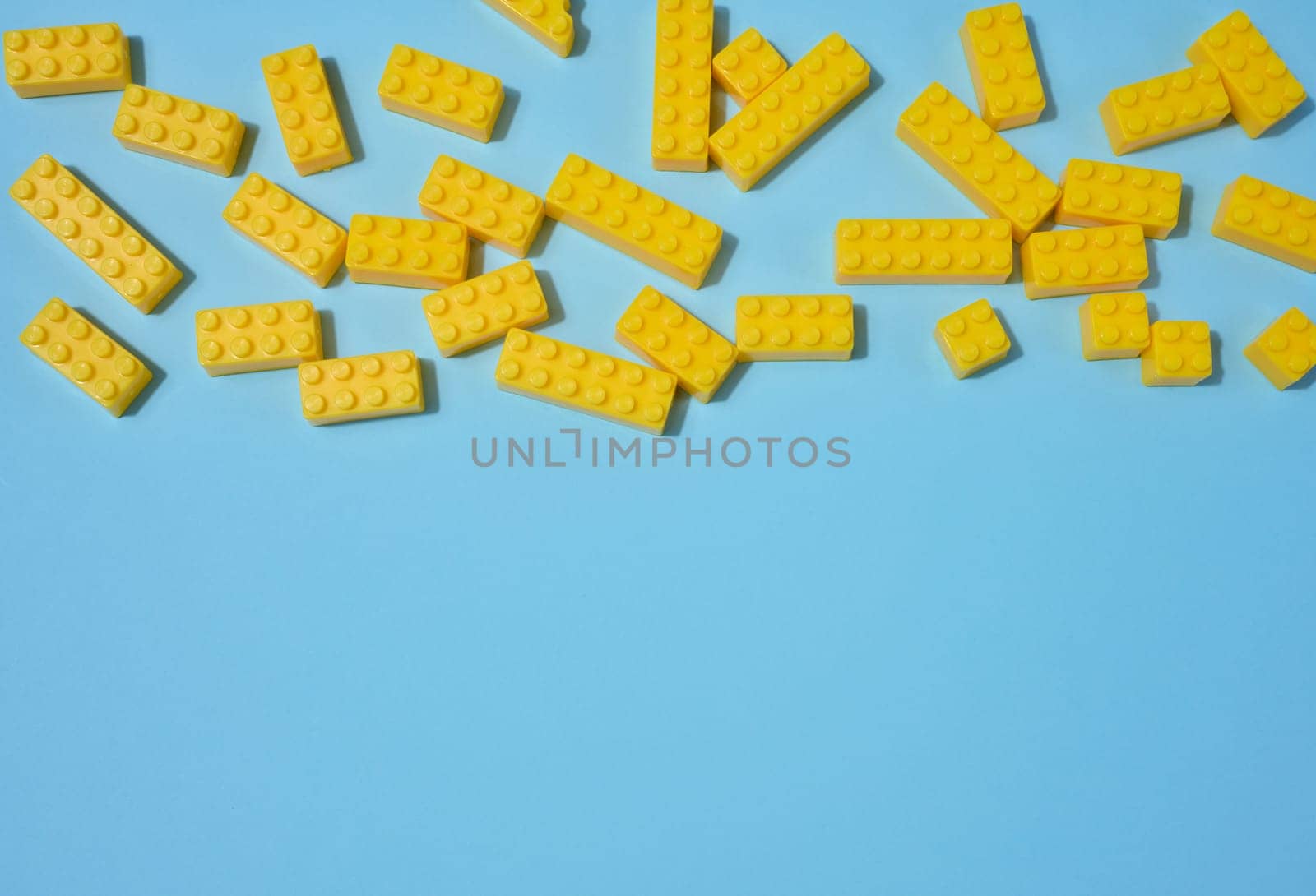 Scattered blue plastic toy building bricks on a solid yellow background. Play, construction, education or creative concept