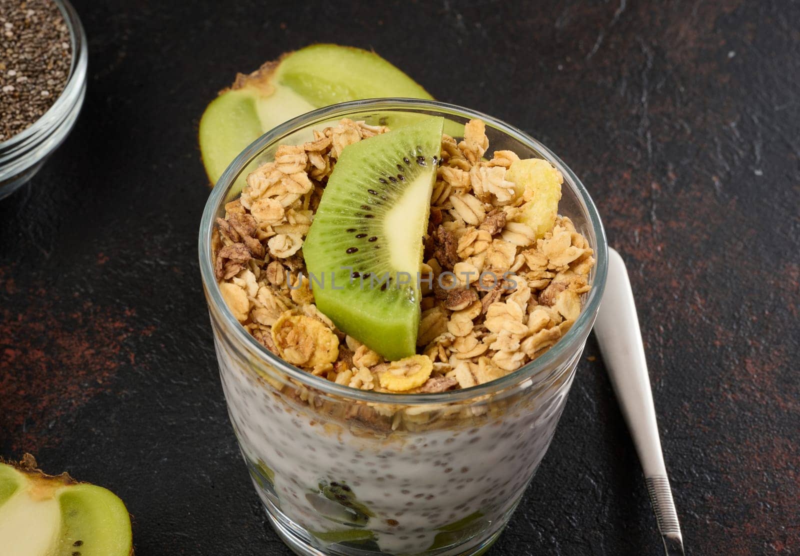 Glass of chia seed pudding layered with kiwi, topped with granola 
