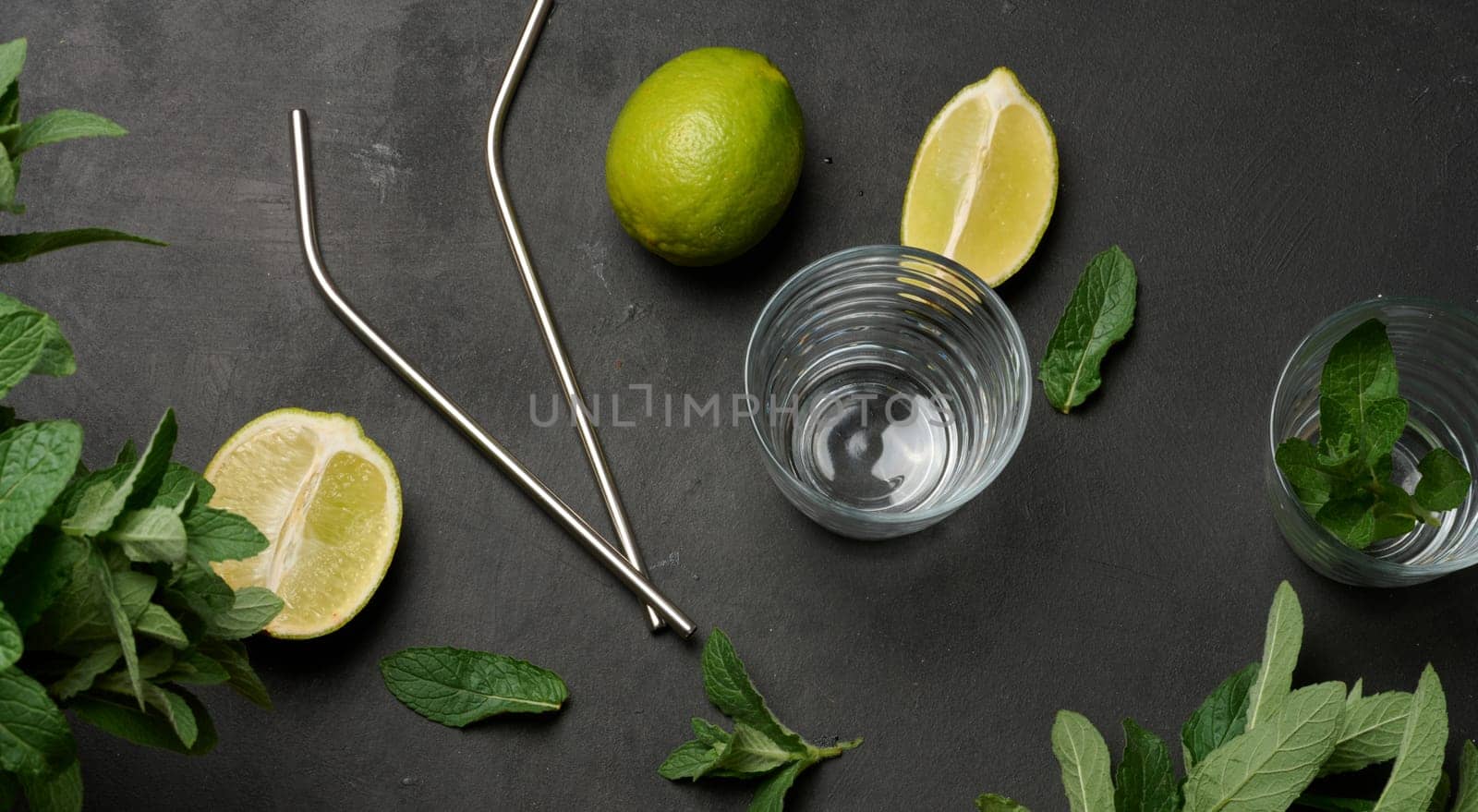 Bunch of fresh green mint, lime slices, glasses and metal straws, top view. Cocktail ingredient