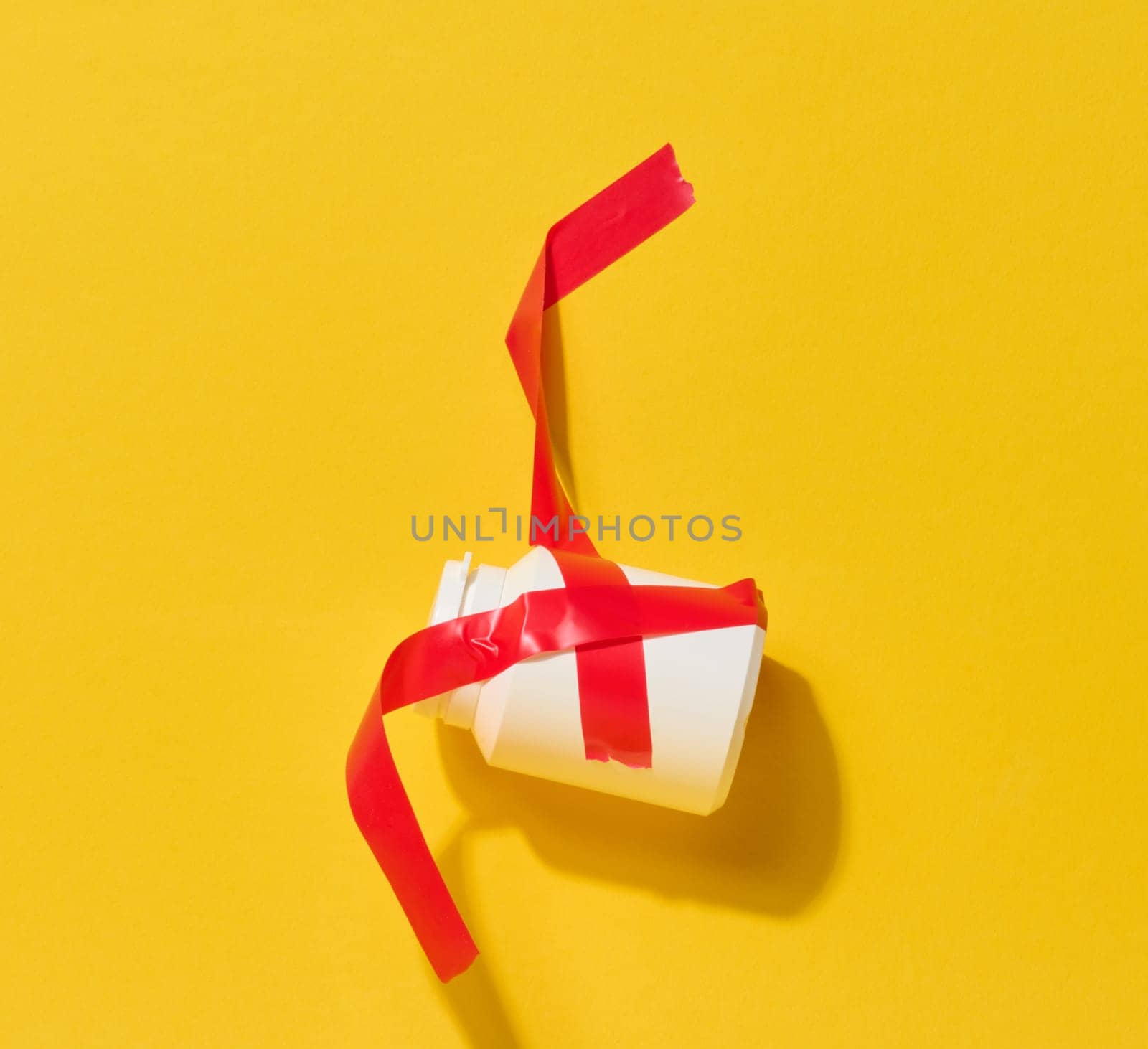 A small white bottle is tightly wrapped and secured with bright red electrical tape against a yellow background