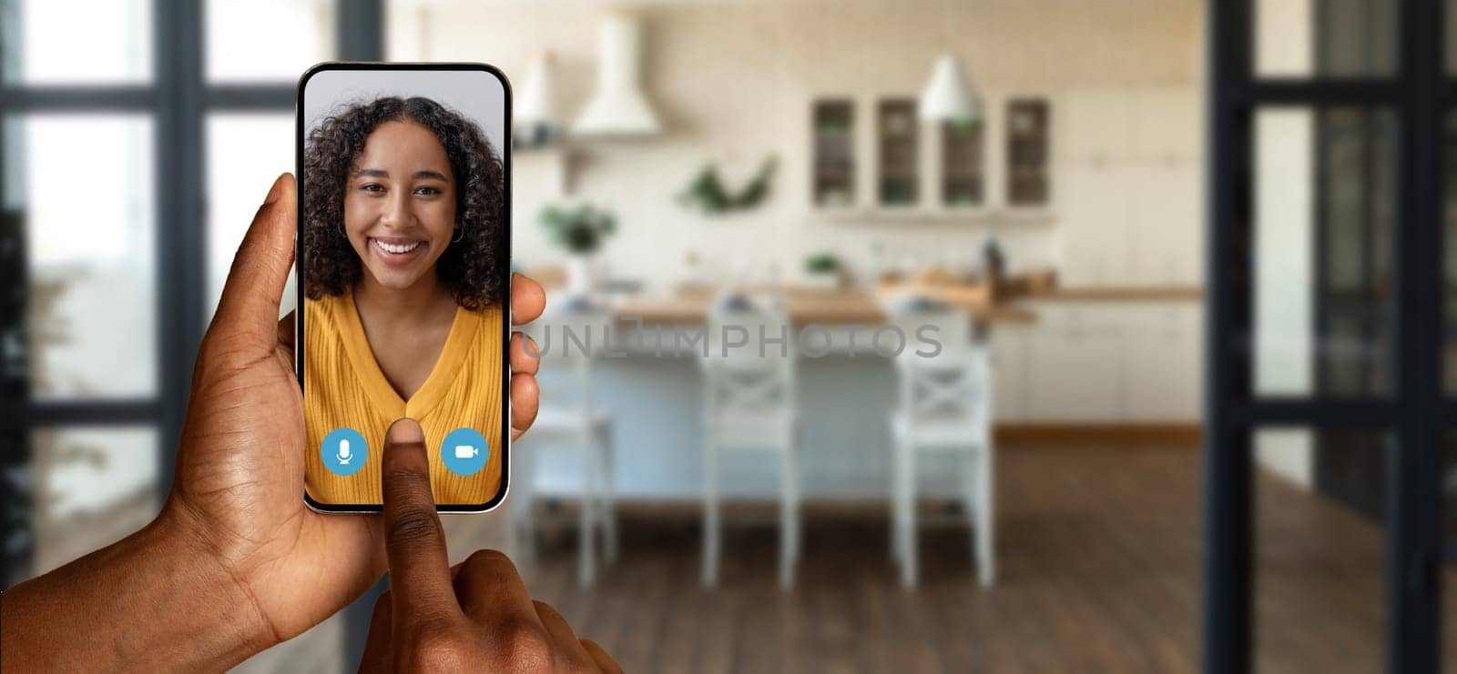 A person using their smartphone to participate in a virtual chat at home. The setting features a modern kitchen with a warm atmosphere, enhancing the online communication experience.