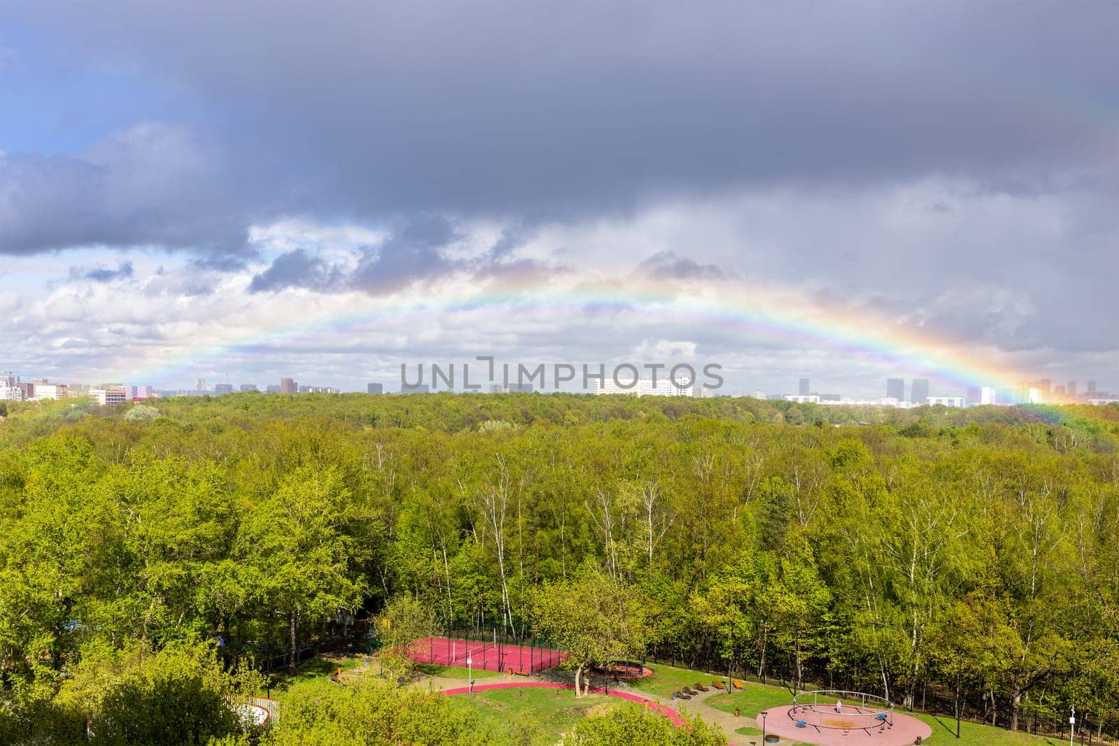 rainbow over green city park and playground after rain on sunny spring day