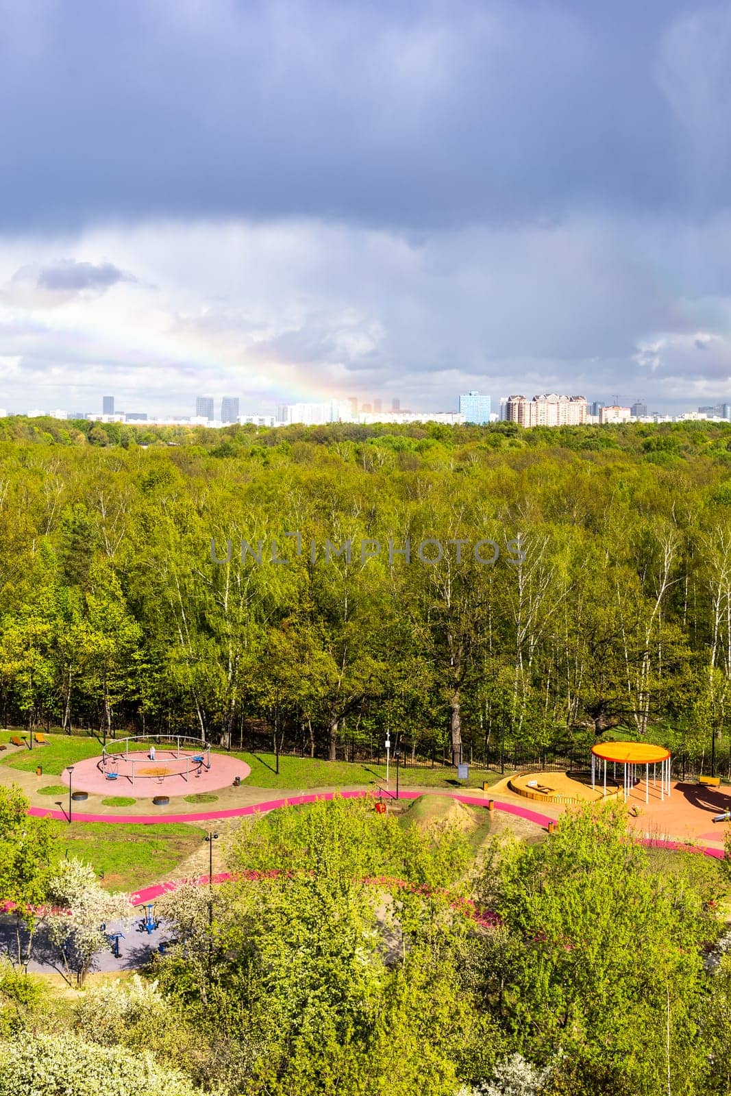 sunlit playground and green city park after rain with rainbow on sunny spring day