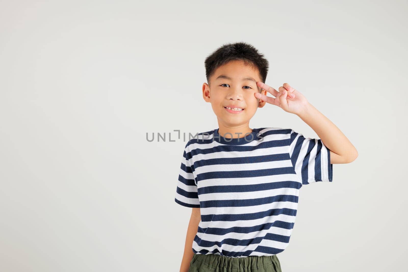 Asian young kid boy showcases optimism and peace by gesturing victory and peace signs in a studio shot with a white background. primary child joyful smile speaks of success, V sign finger