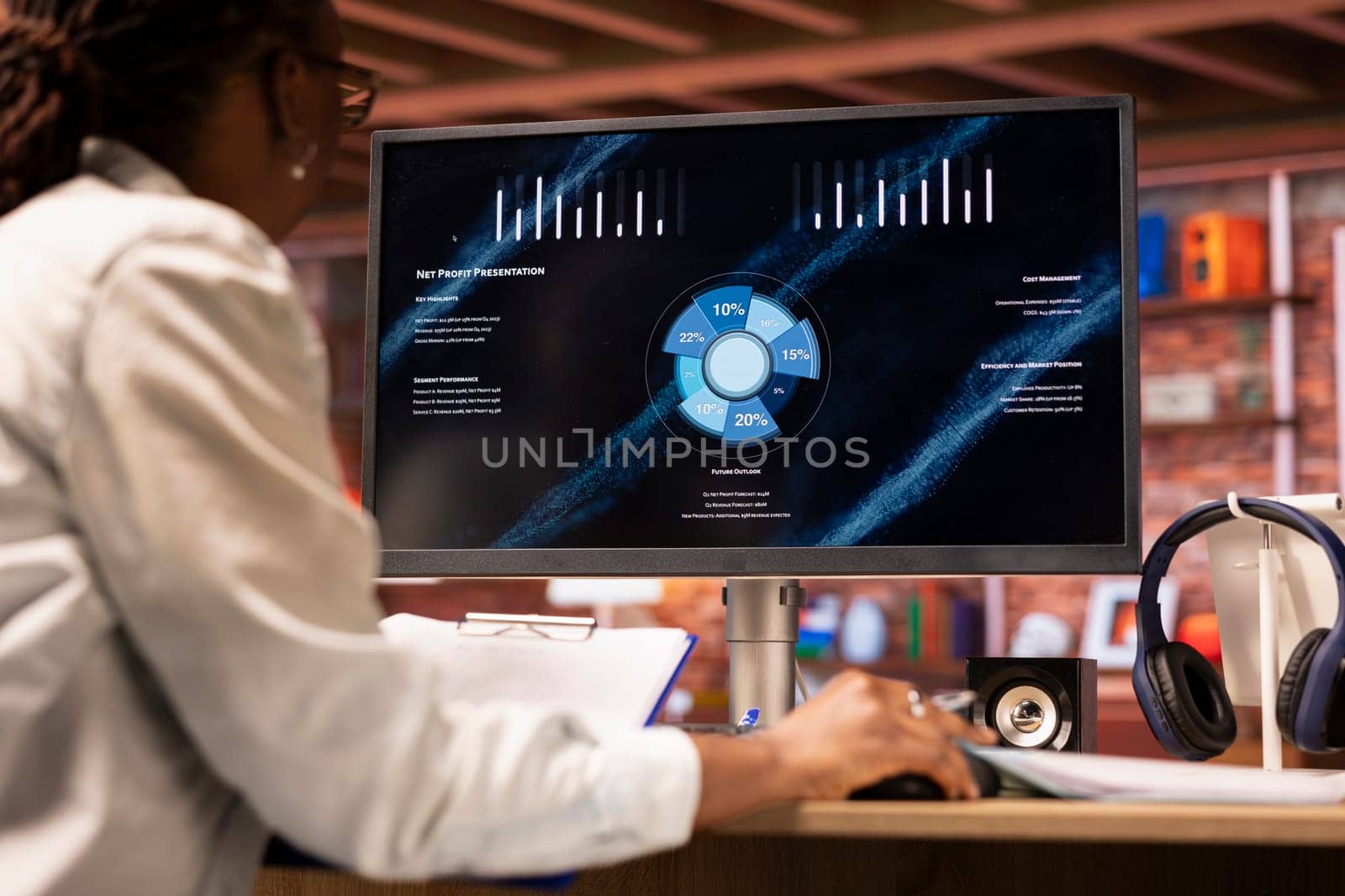 Woman watching business conference on computer screen, looking over statistics on portfolio documents. African american person in apartment looking at business presentation