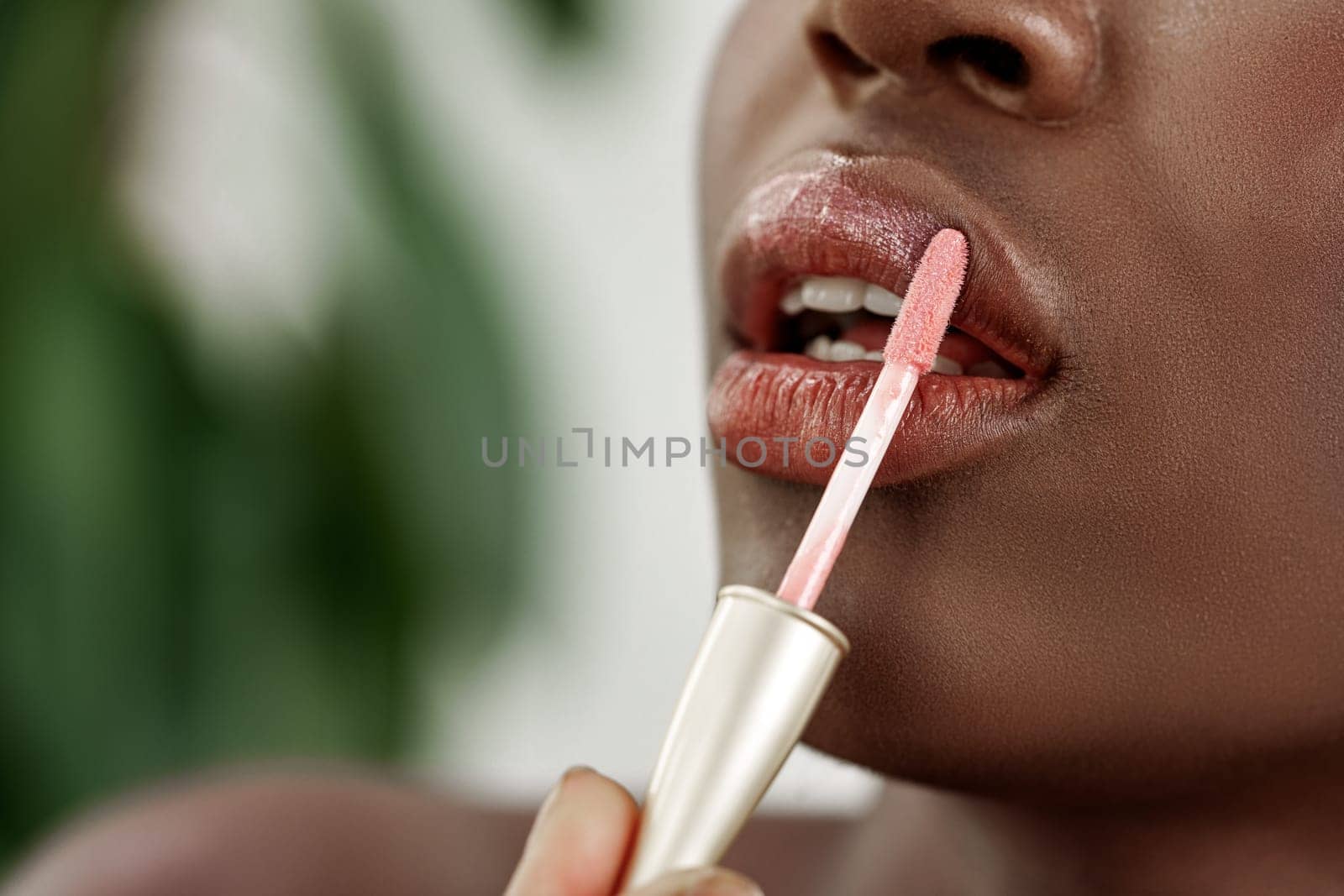 In a well-lit environment, a person applies a soft pink lip gloss to their lips. The focus is on the careful application, highlighting the smooth texture and vibrant color.