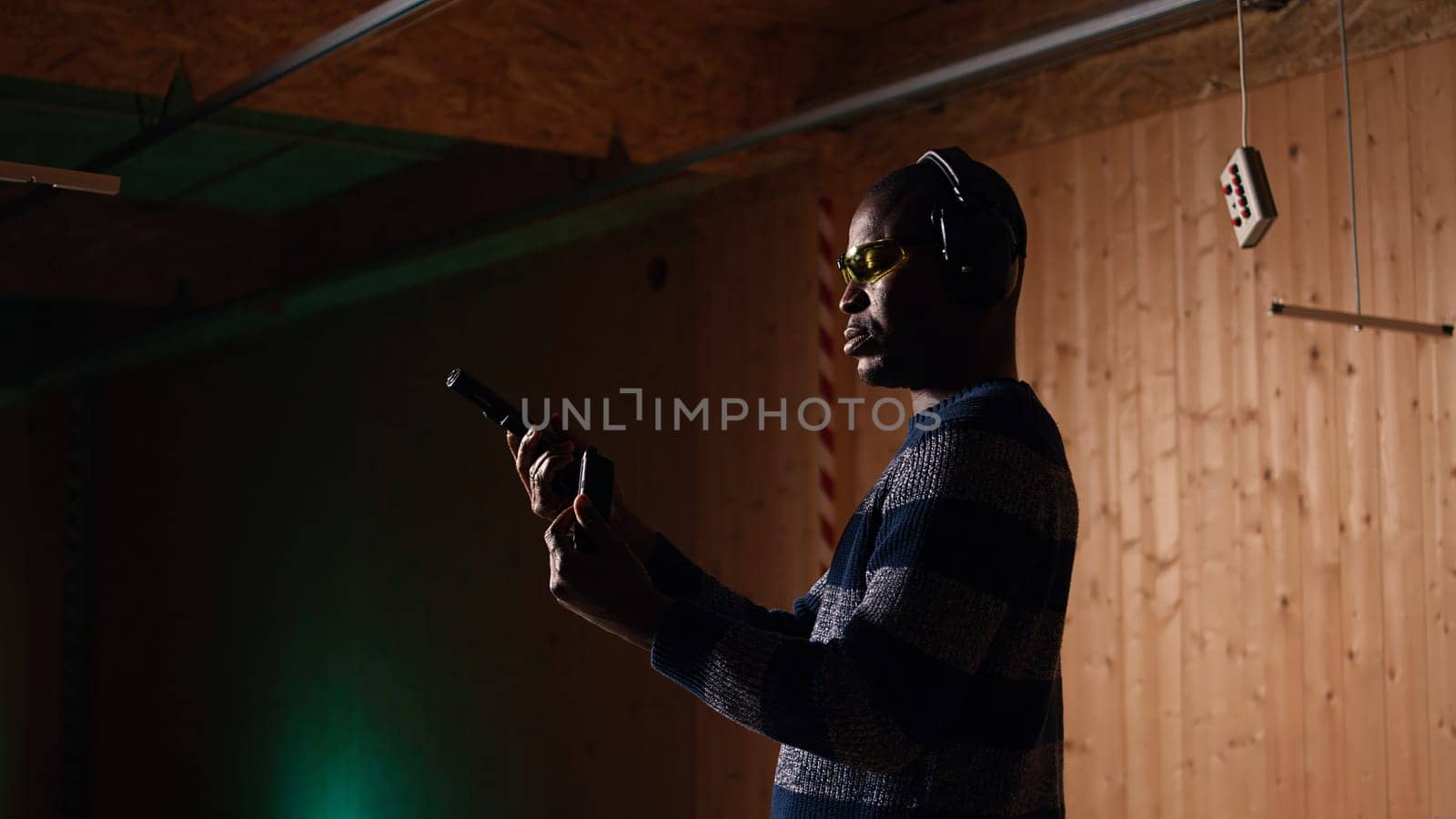 Portrait of smiling man doing training in shooting range, learning proper pistol holding etiquette and having fun. Cheerful gun hobbyist practicing with weapons, wearing protective eyewear, camera A