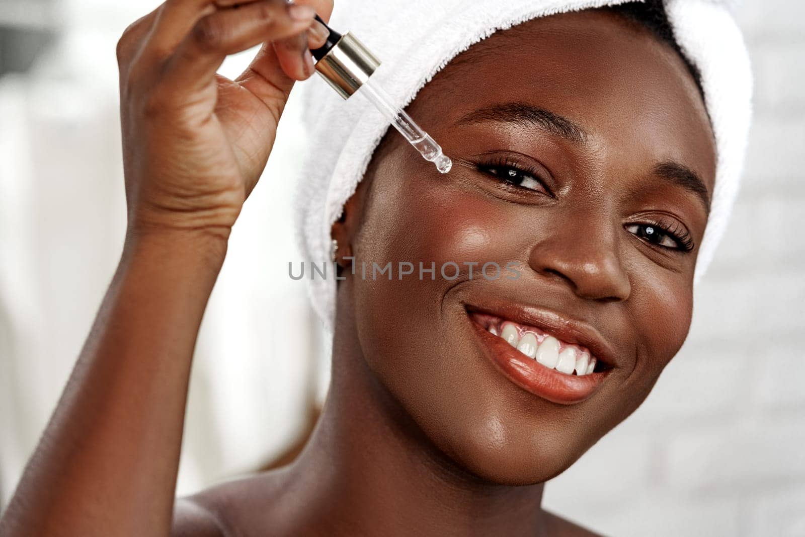 A joyful woman smiles while applying a serum to her face in a bright, modern bathroom. The atmosphere is fresh and uplifting, highlighting self-care and beauty.