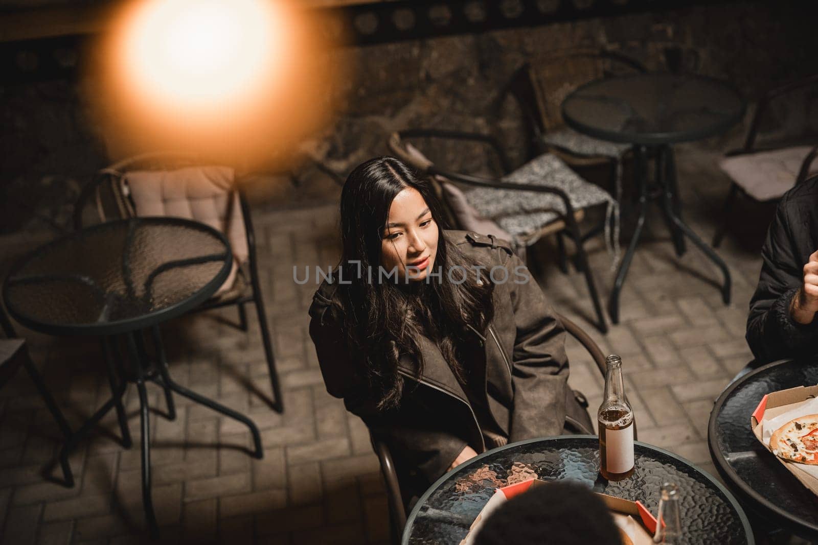 Friends gather in a cozy outdoor cafe during the evening to enjoy pizza and drinks. Warm light creates a relaxed atmosphere for their lively conversation.