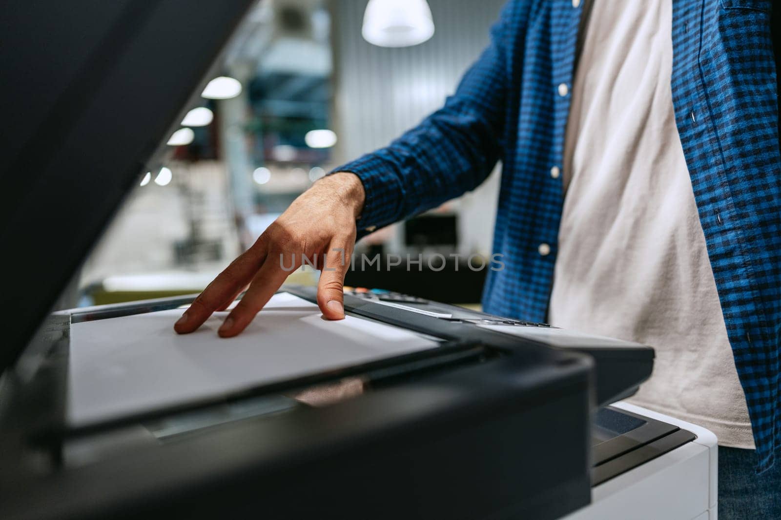 Individual is using a printer to make copies of documents in a contemporary office space. The setting includes various office equipment and lighting.