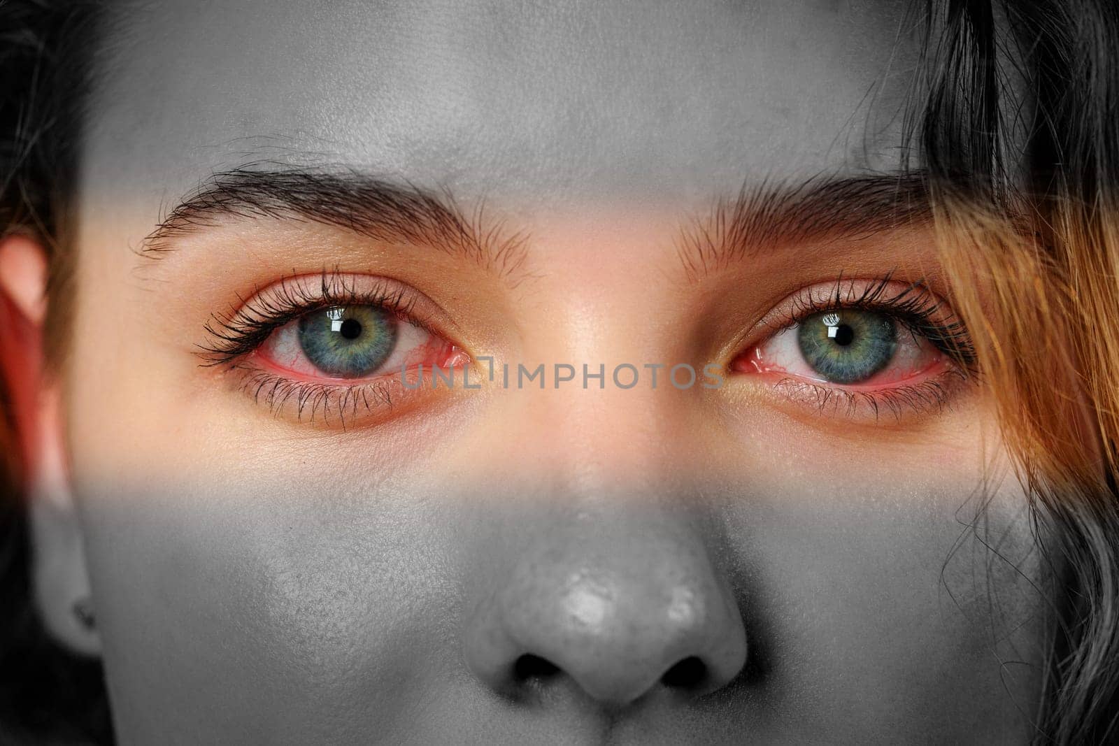 A close-up of a person's face reveals bright blue eyes that stand out against a monochrome background. The play of light creates a dramatic effect on their features.