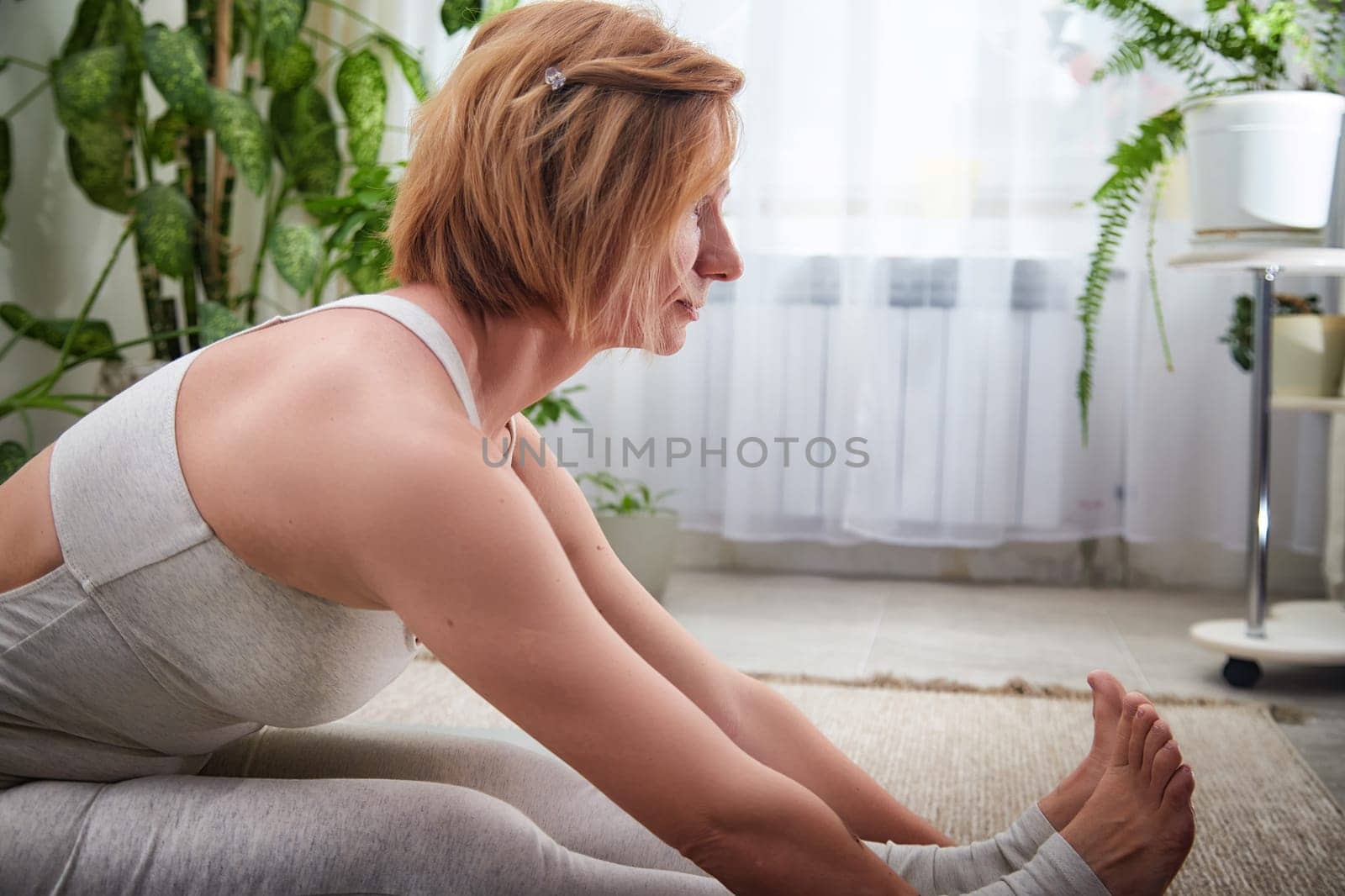 Individual focuses on deep stretching techniques during a yoga session in a serene indoor space surrounded by greenery.