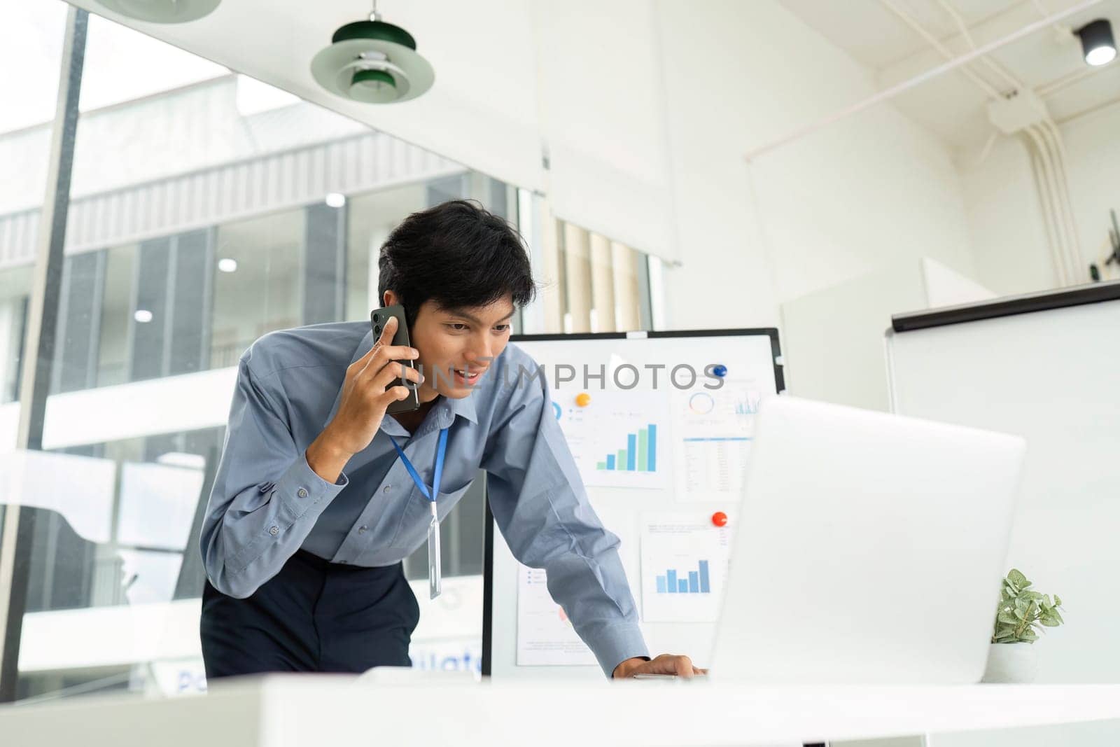 A focused businessman speaks on the phone while analyzing data on a laptop, showcasing productivity in a modern office.