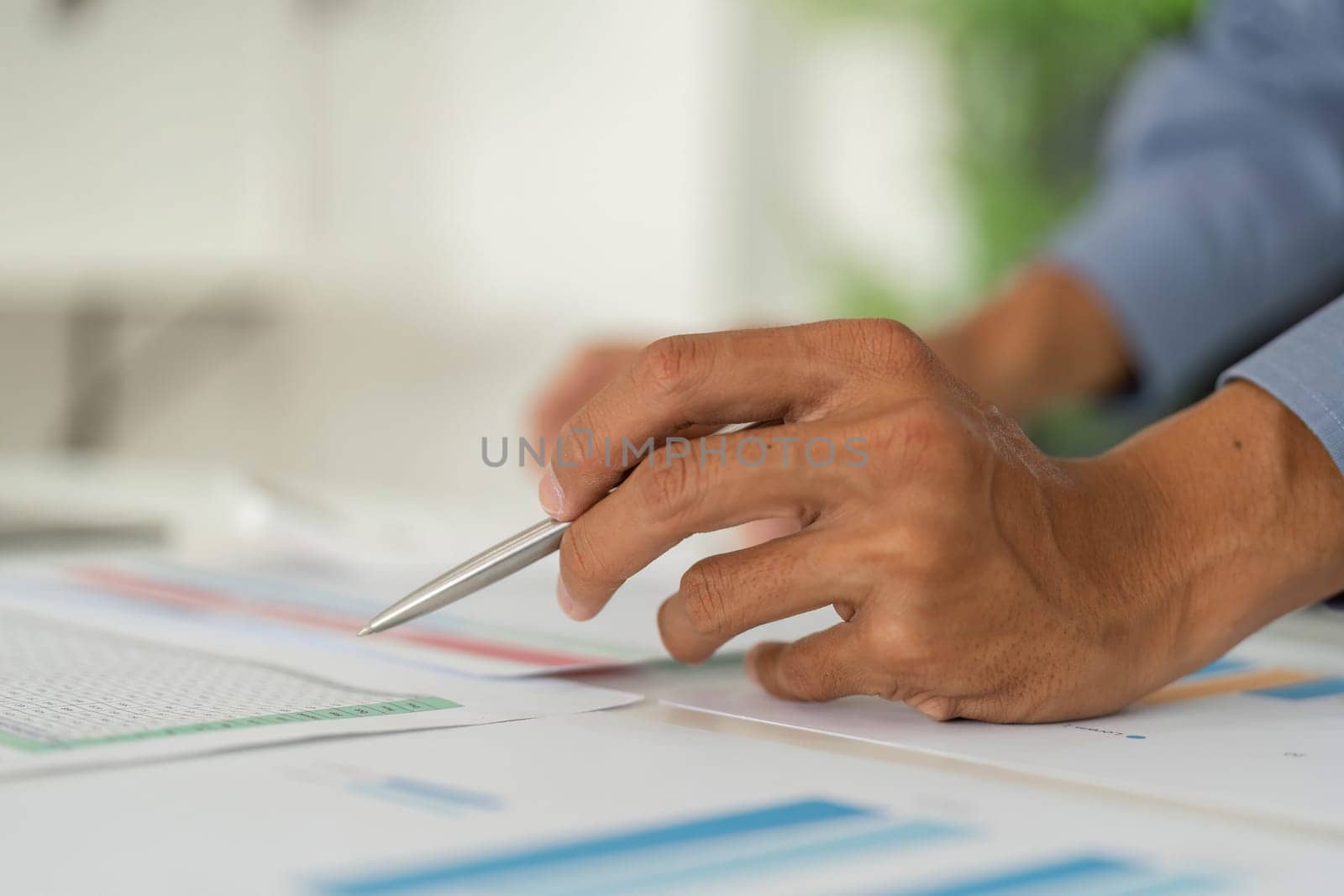 A close-up view of a professional's hand holding a pen, reviewing detailed reports and charts on a desk.