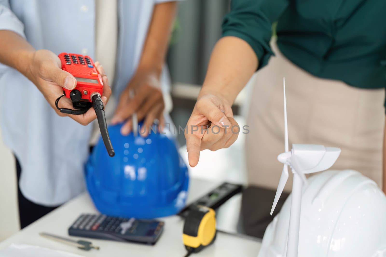 Colleagues measuring and discussing safety equipment while emphasizing project planning and communication in a modern workspace.