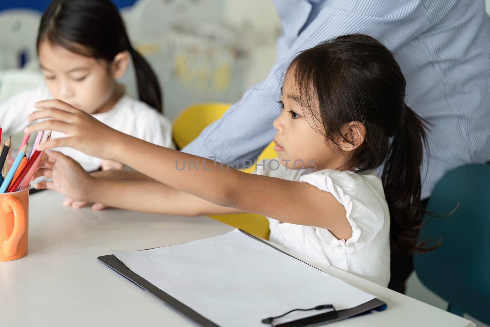 Two young girls interact while reaching for art supplies, promoting creativity and collaboration in a classroom setting.