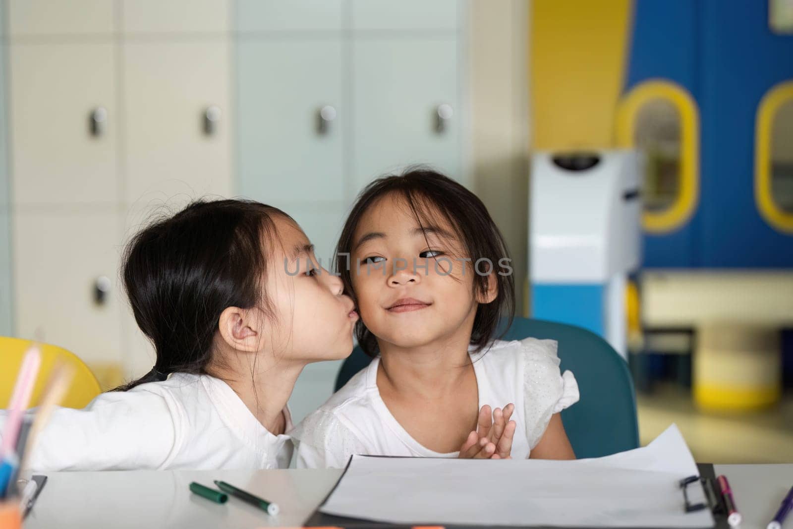 Two young girls share a sweet moment in class, highlighting friendship and emotional connection while learning together.