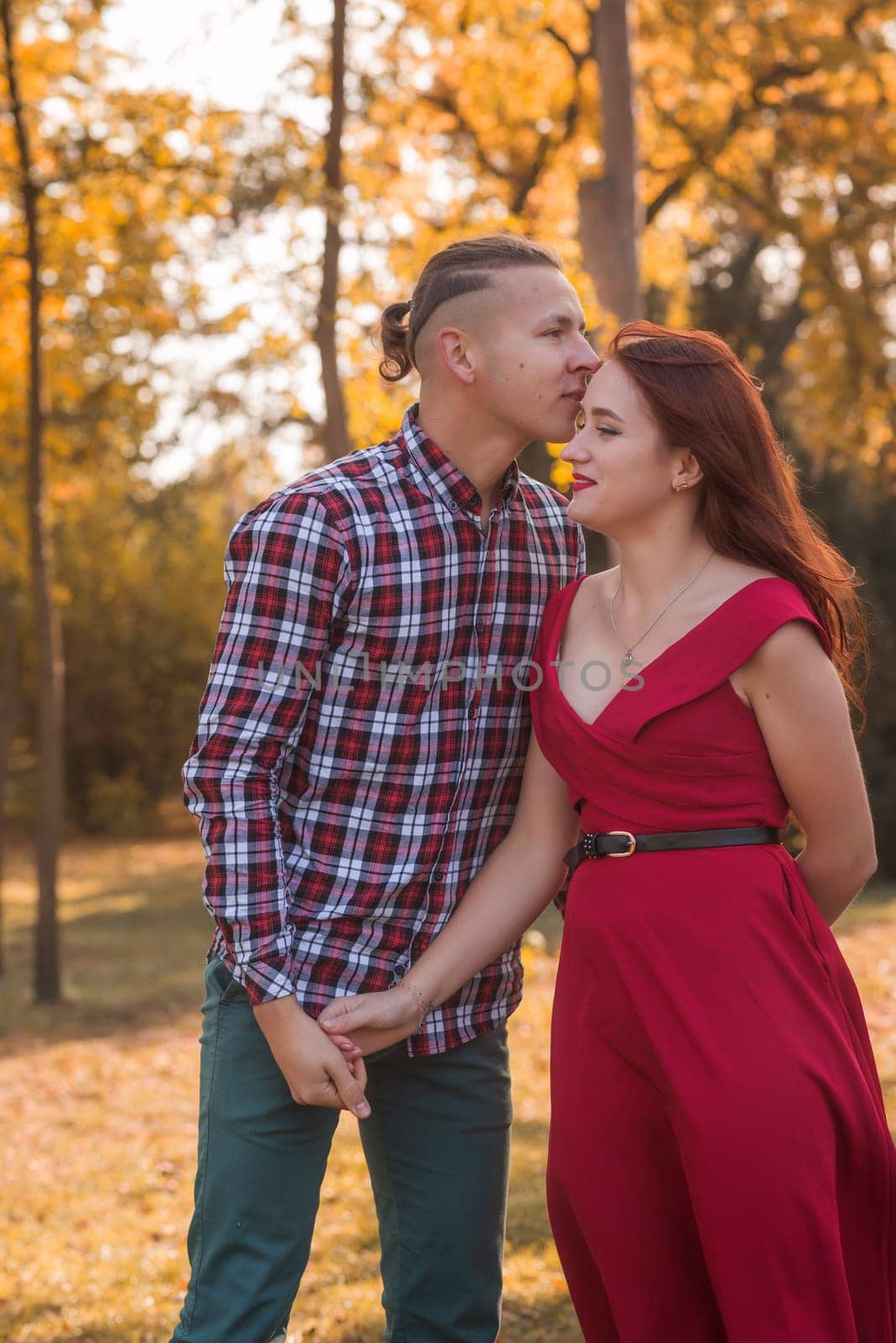 Portrait of a young couple in love kissing and hugging in an autumn park. Girl in a red dress against the backdrop of golden autumn. Concept of romance, falling in love