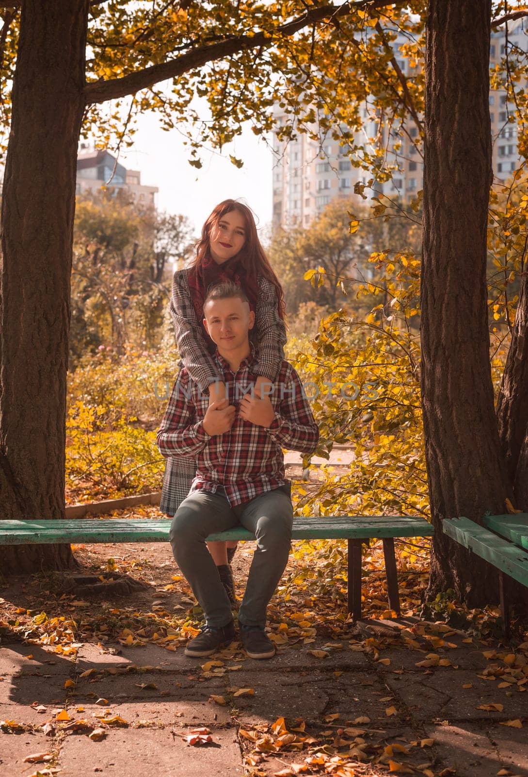 A couple in love in an autumn park, sitting on a bench, hugging and holding hands. General plan. A young couple looking at the camera.