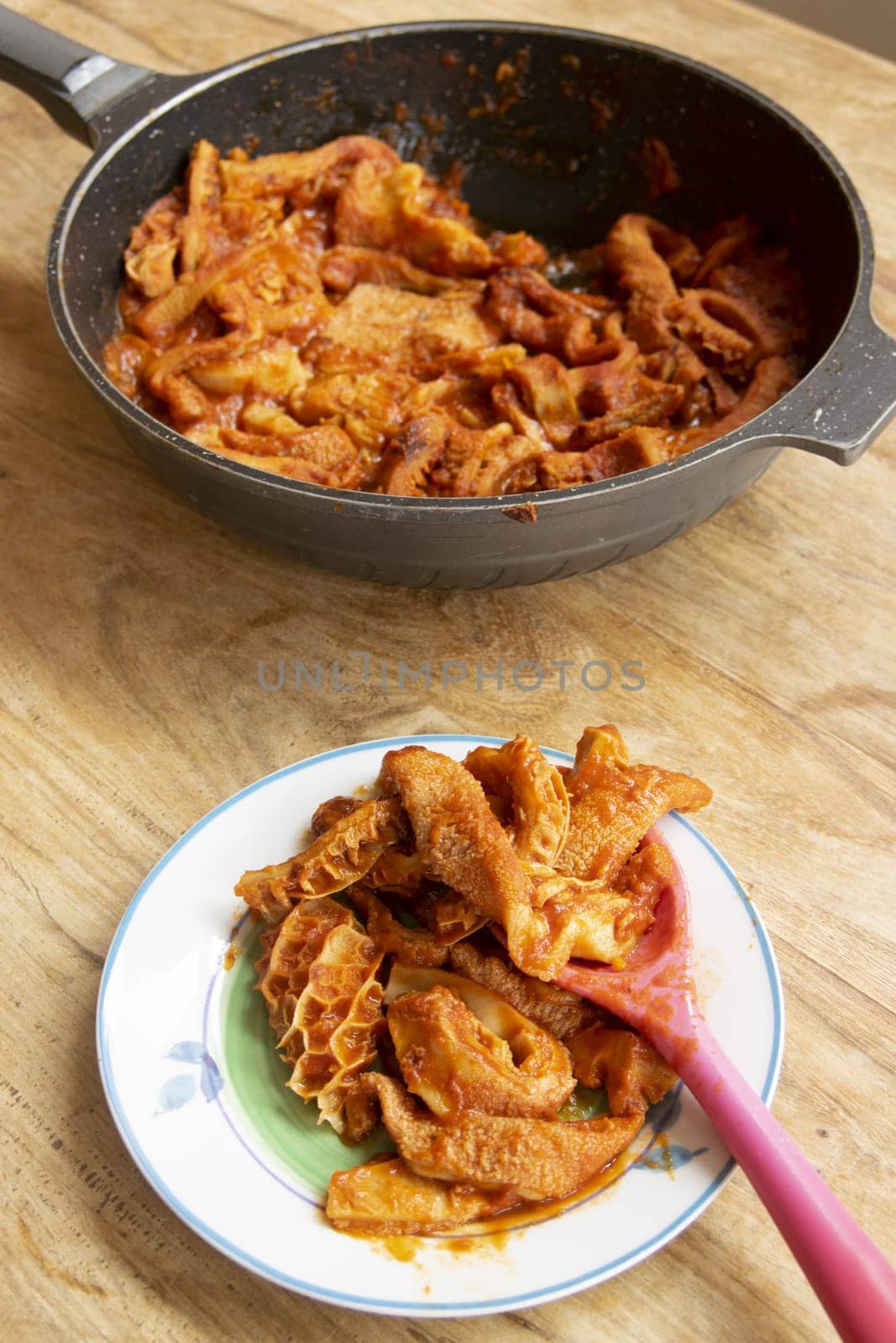 Traditional Roman Trippa alla Romana on a plate, with more cooking in pan. Classic Italian comfort food: tender tripe in rich tomato sauce with herbs