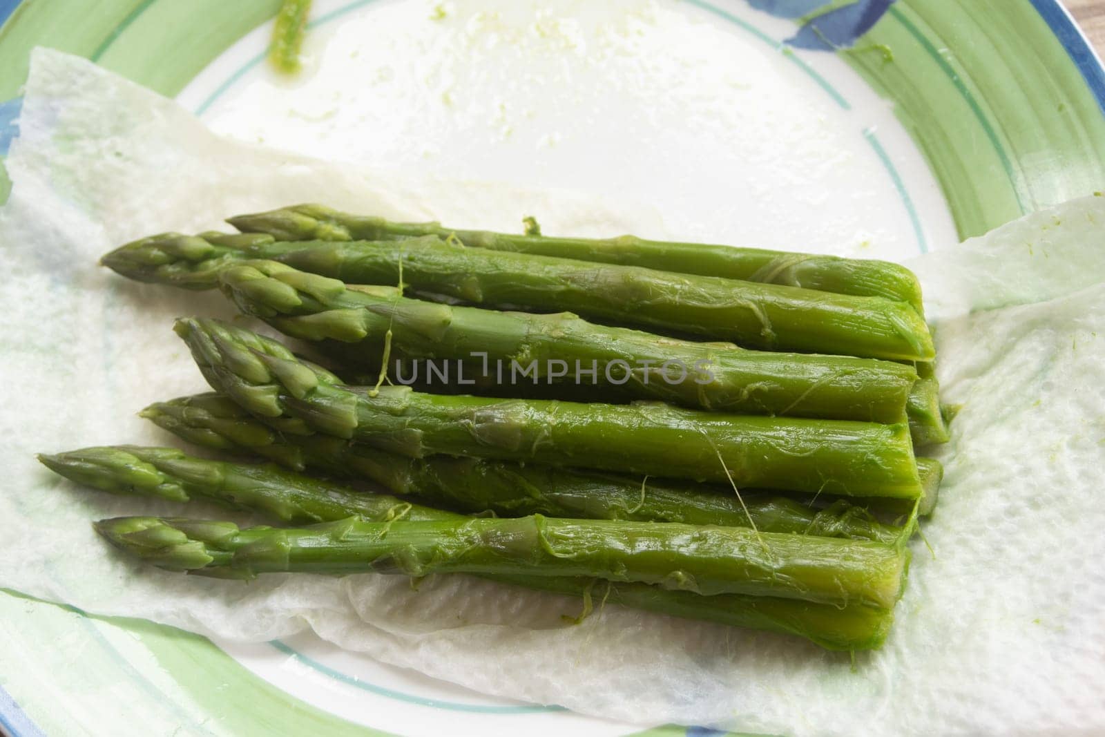 A bunch of freshly steamed asparagus spears rests on a metal rack over a green and white plate, highlighting their vibrant color and freshness