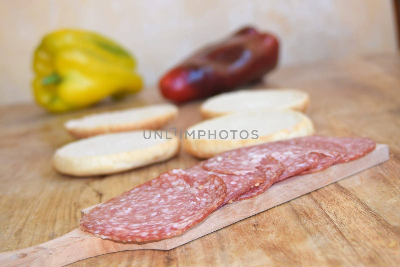 Thin slices of dry-cured salami on a wooden board with fresh bread and green onions.
