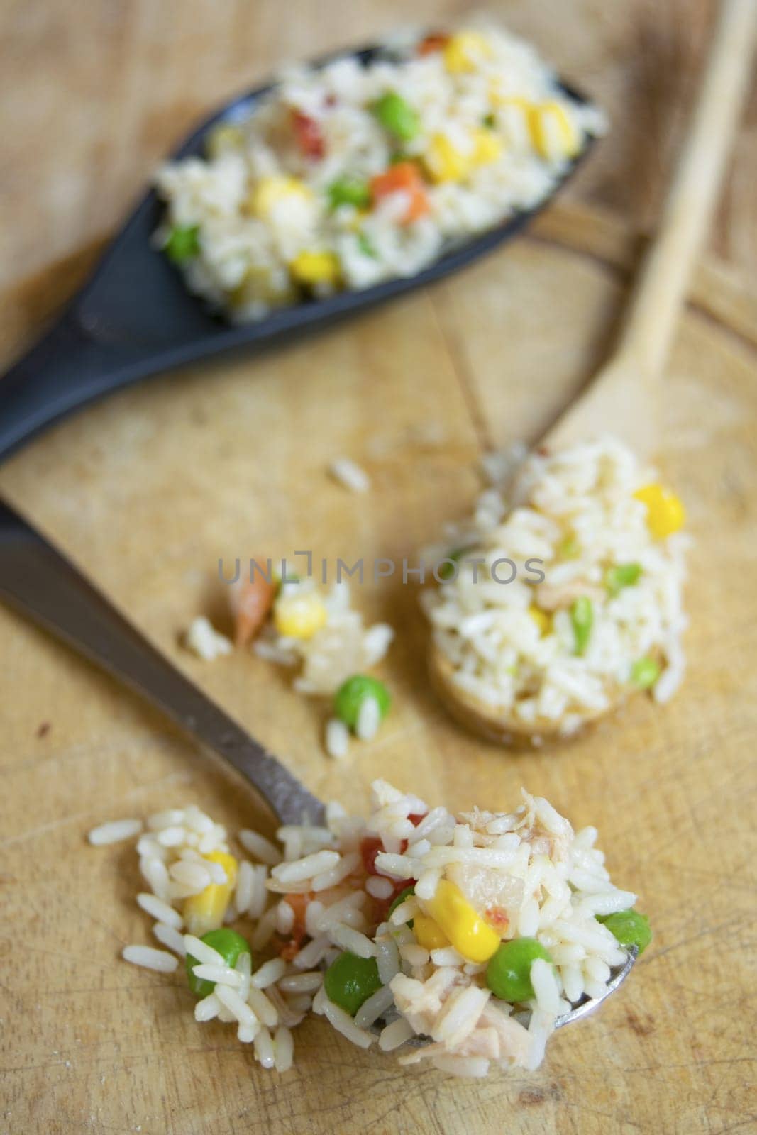 A vibrant vegetable rice salad with peas, corn, and tomatoes, surrounded by fresh ingredients on a rustic wooden surface