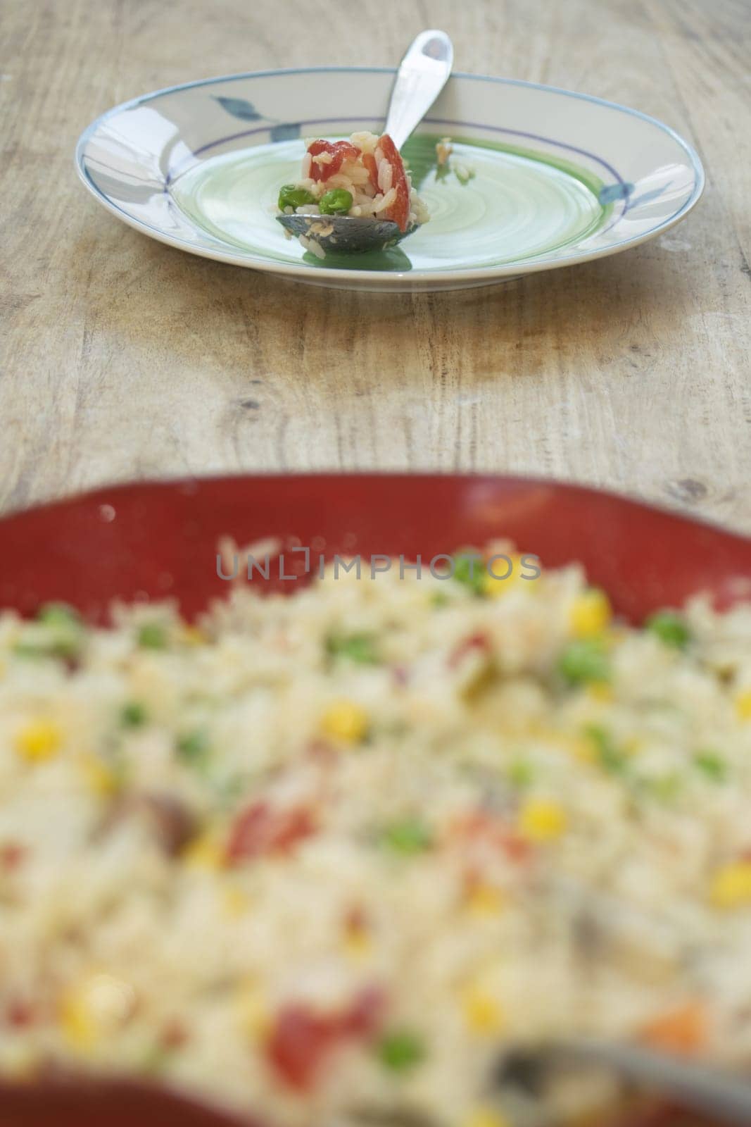 A vibrant vegetable rice salad with peas, corn, and tomatoes, surrounded by fresh ingredients on a rustic wooden surface