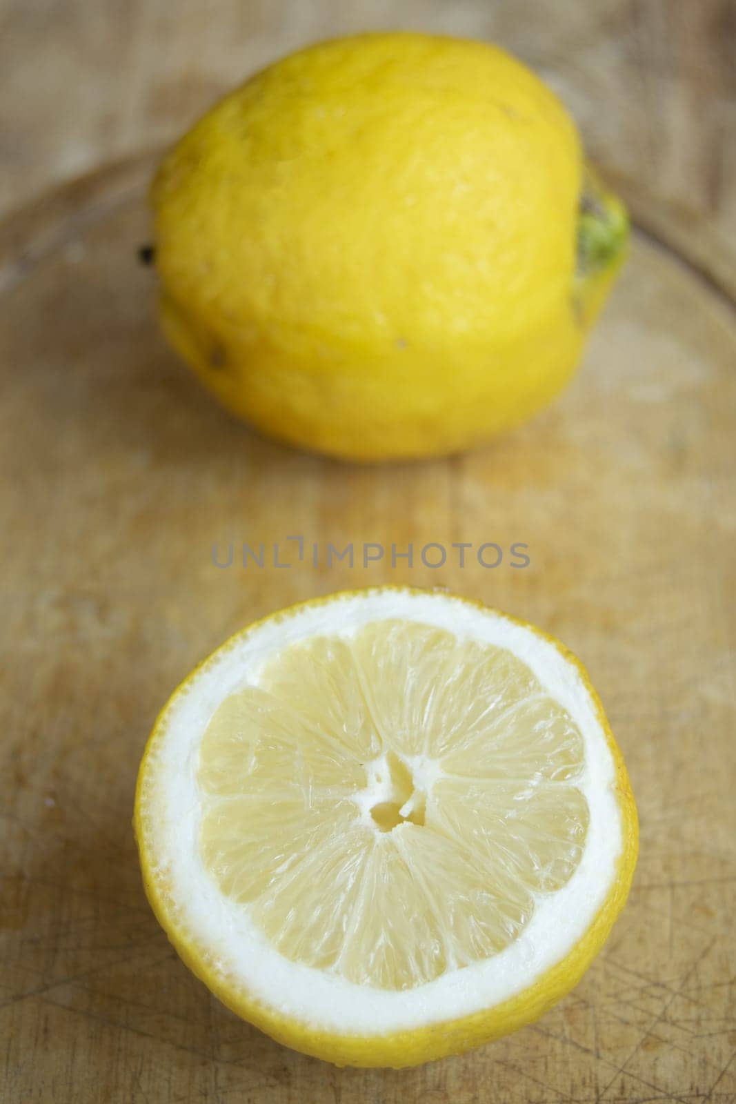 Two bright yellow lemons, one whole and one halved to reveal its juicy interior, on a rustic wooden surface